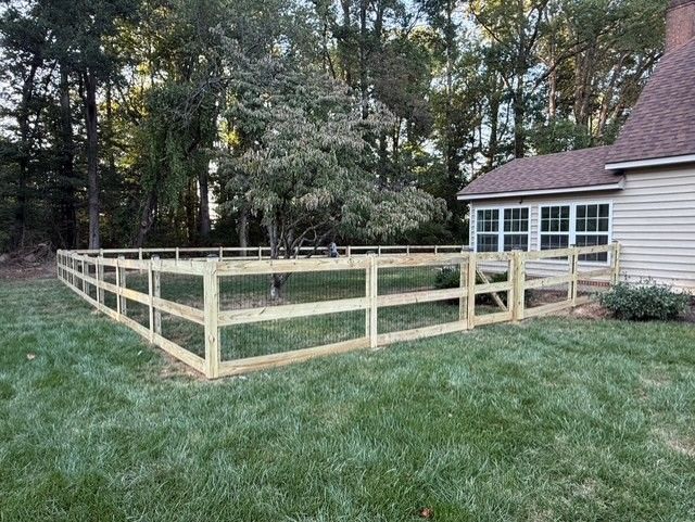 Wooden fence enclosing a grassy yard near a house and trees.