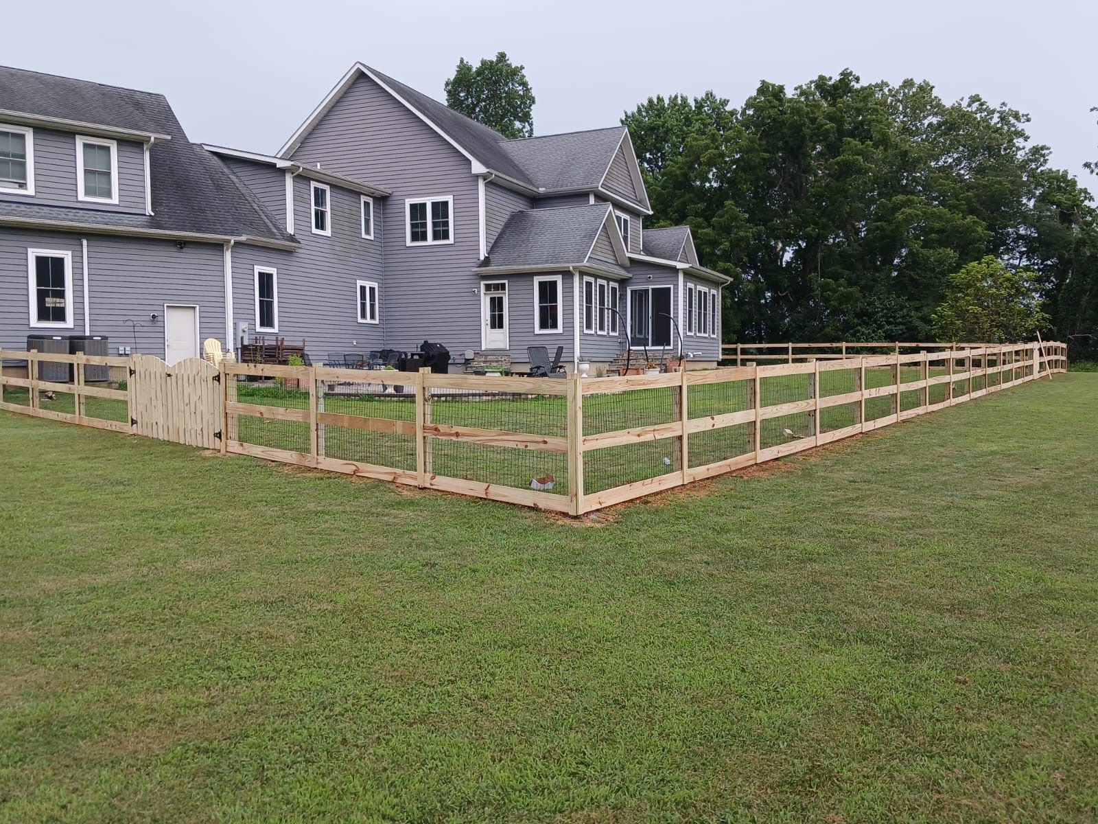 Two-story house with a wooden fence in the backyard; green grass and cloudy sky.