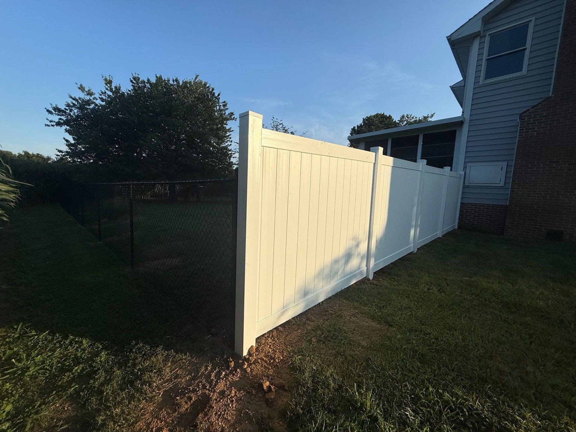White vinyl fence next to a house with a black chain link fence in the background.