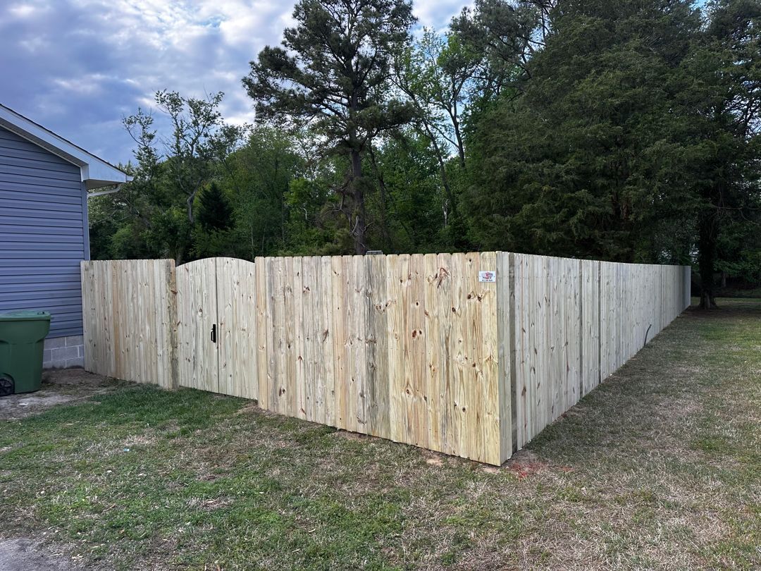 Wooden fence surrounding a grassy yard with trees in the background under a cloudy sky.