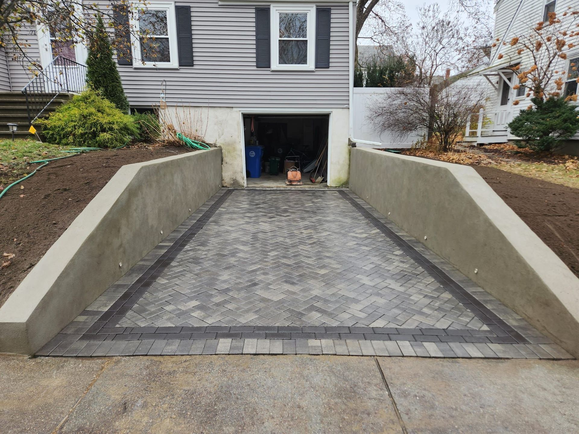 Concrete driveway descending to a garage under a house, bordered by low retaining walls.
