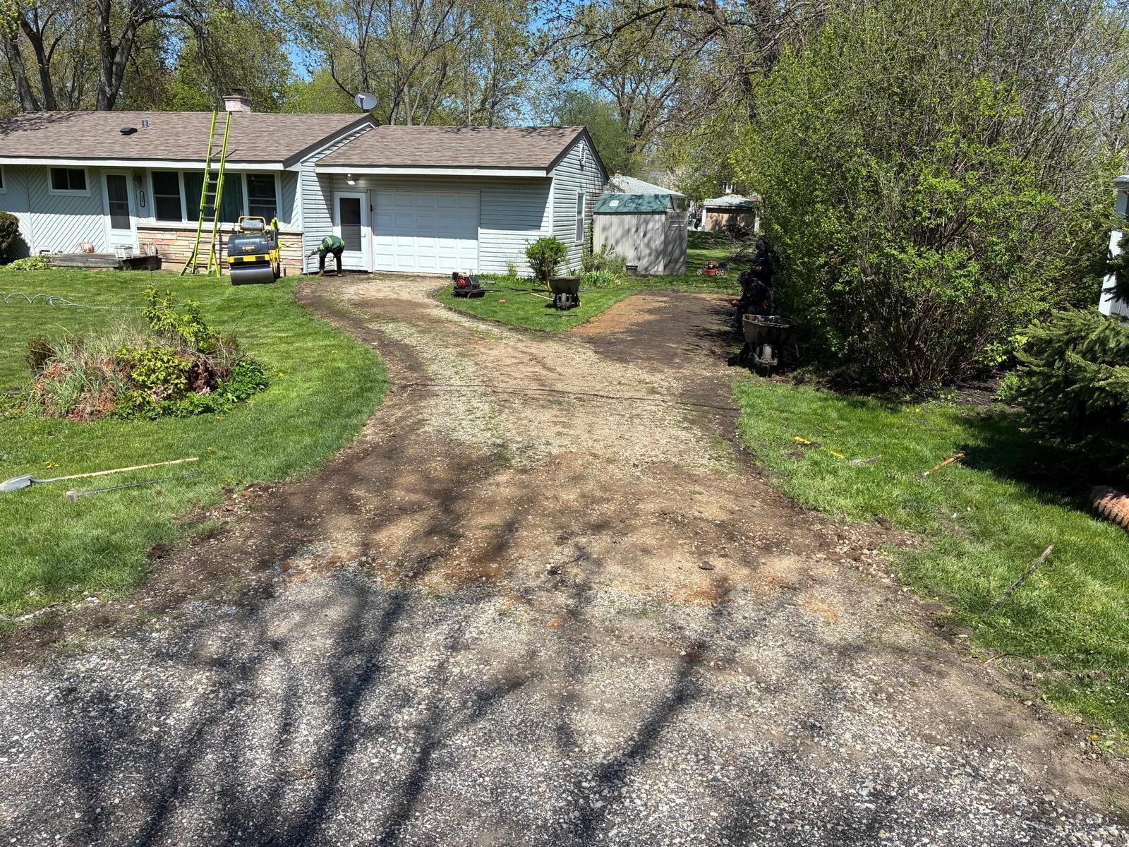Front yard with a curved gravel driveway leading to a white house and garage, surrounded by green trees and grass