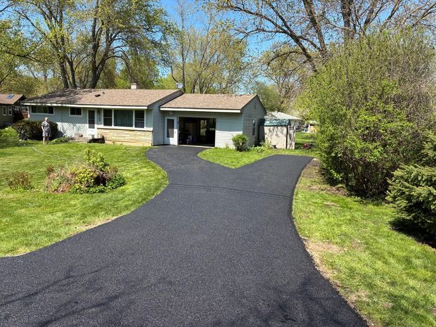 Suburban house with a newly paved black driveway and green lawn under trees