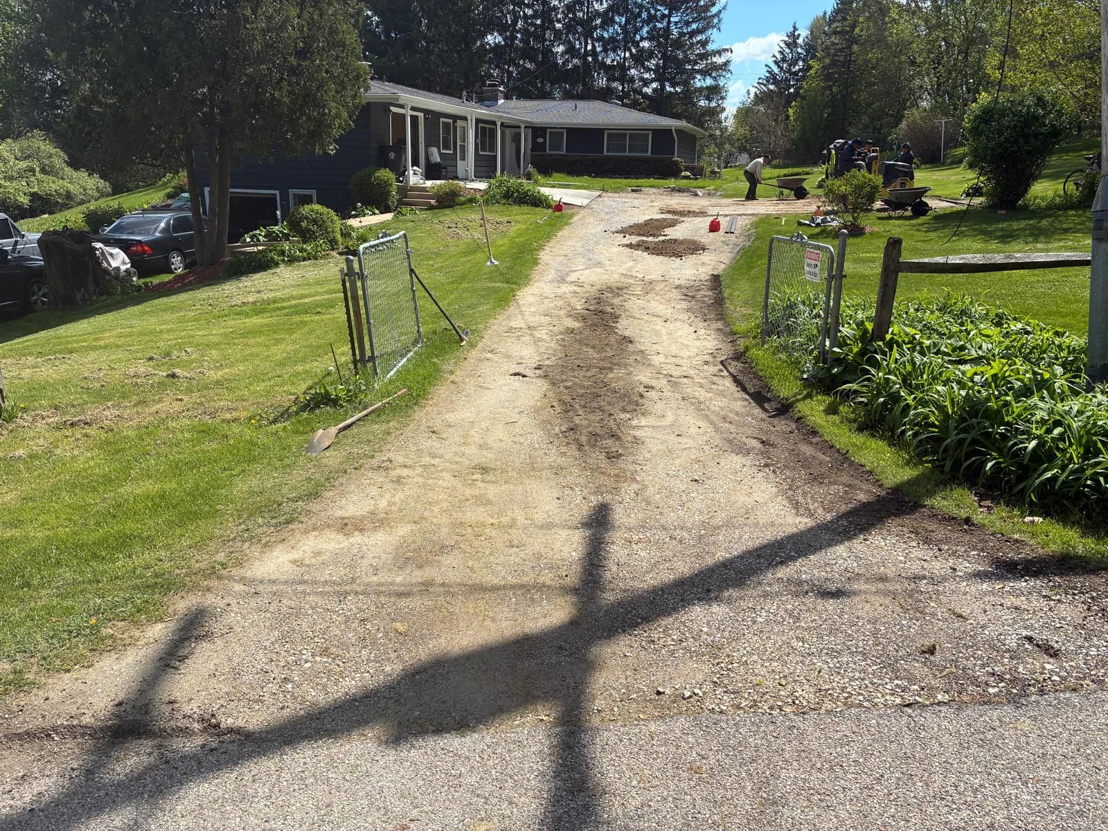 Gravel driveway leading to a house with green lawn and trees on a sunny day