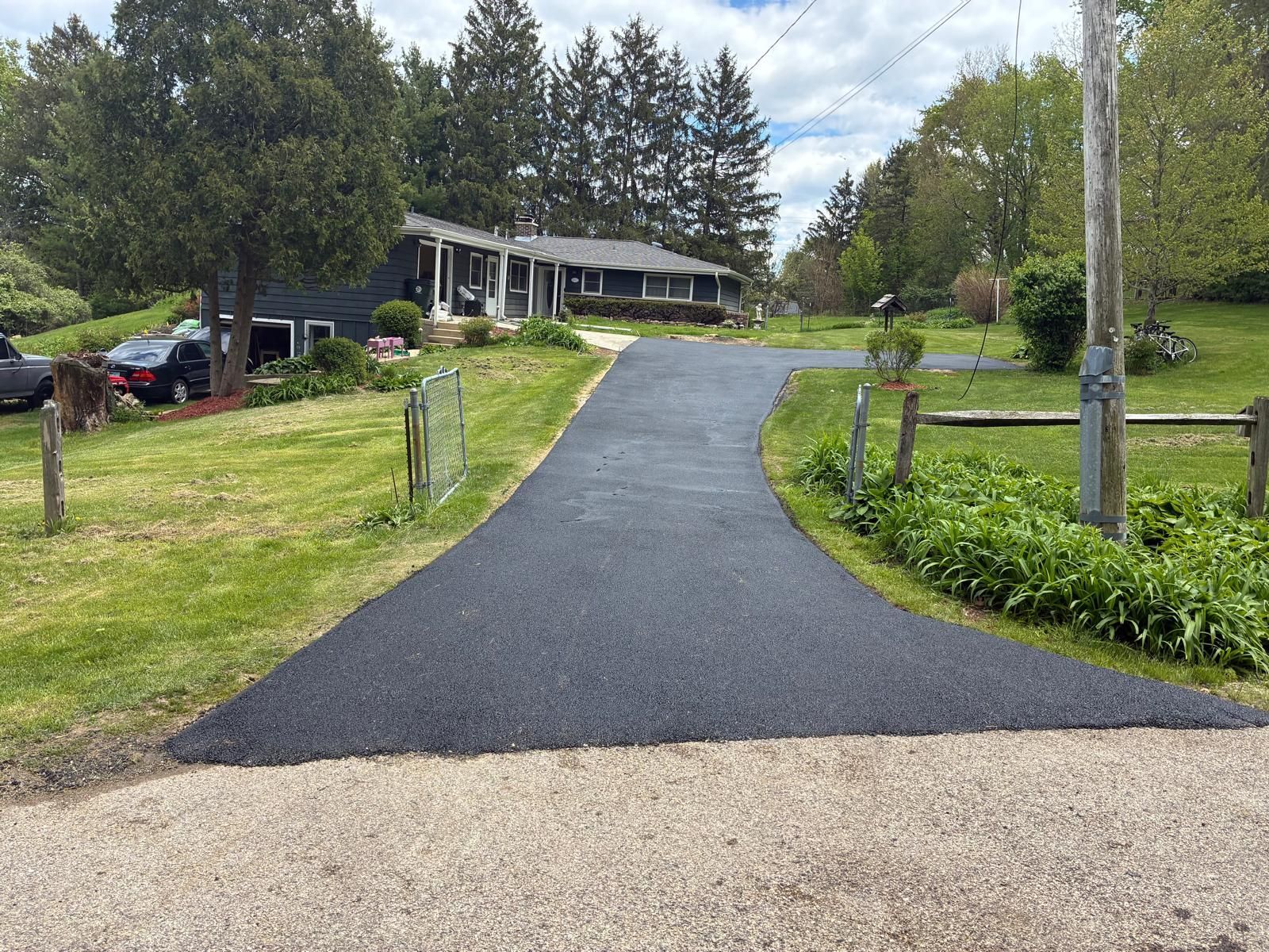 Freshly paved driveway curving toward a house surrounded by trees and grass.