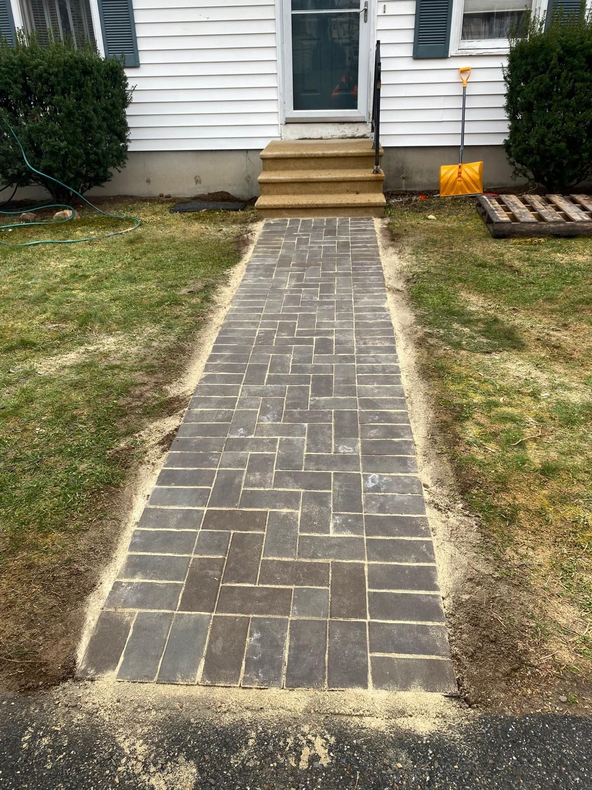 Brick walkway leading to a white house’s front steps, with patches of grass on both sides.