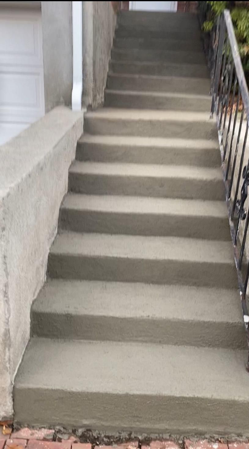 Outdoor concrete staircase beside a white wall and black metal railing