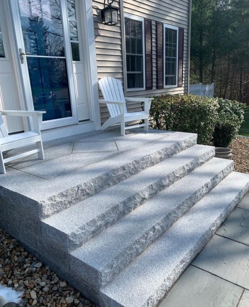 Front porch with gray stone steps, white railings, and chairs beside a house exterior