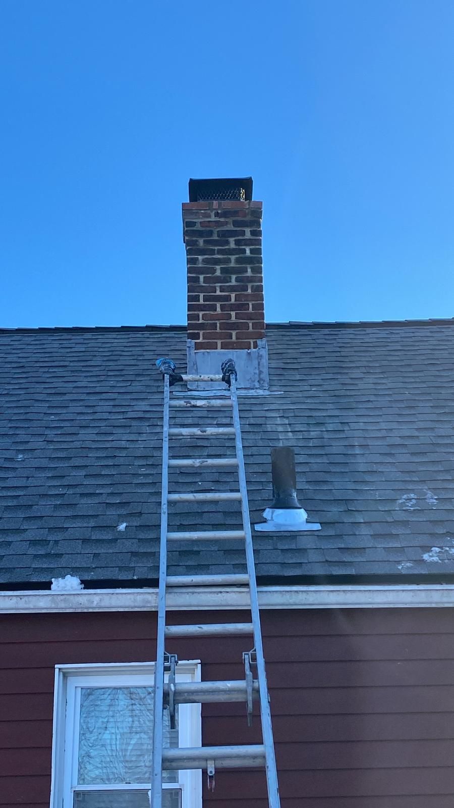 Ladder leaning against a house roof beneath a brick chimney on a shingled rooftop