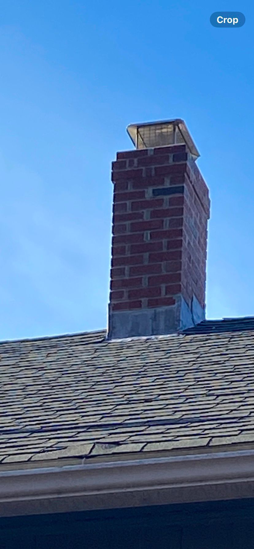 Brick chimney above a shingled roof against a clear blue sky
