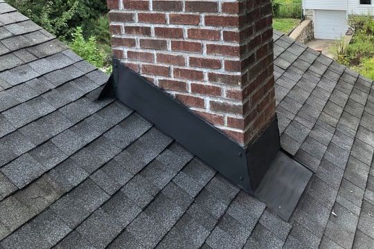 Roof around brick chimney with black metal flashing on gray shingles