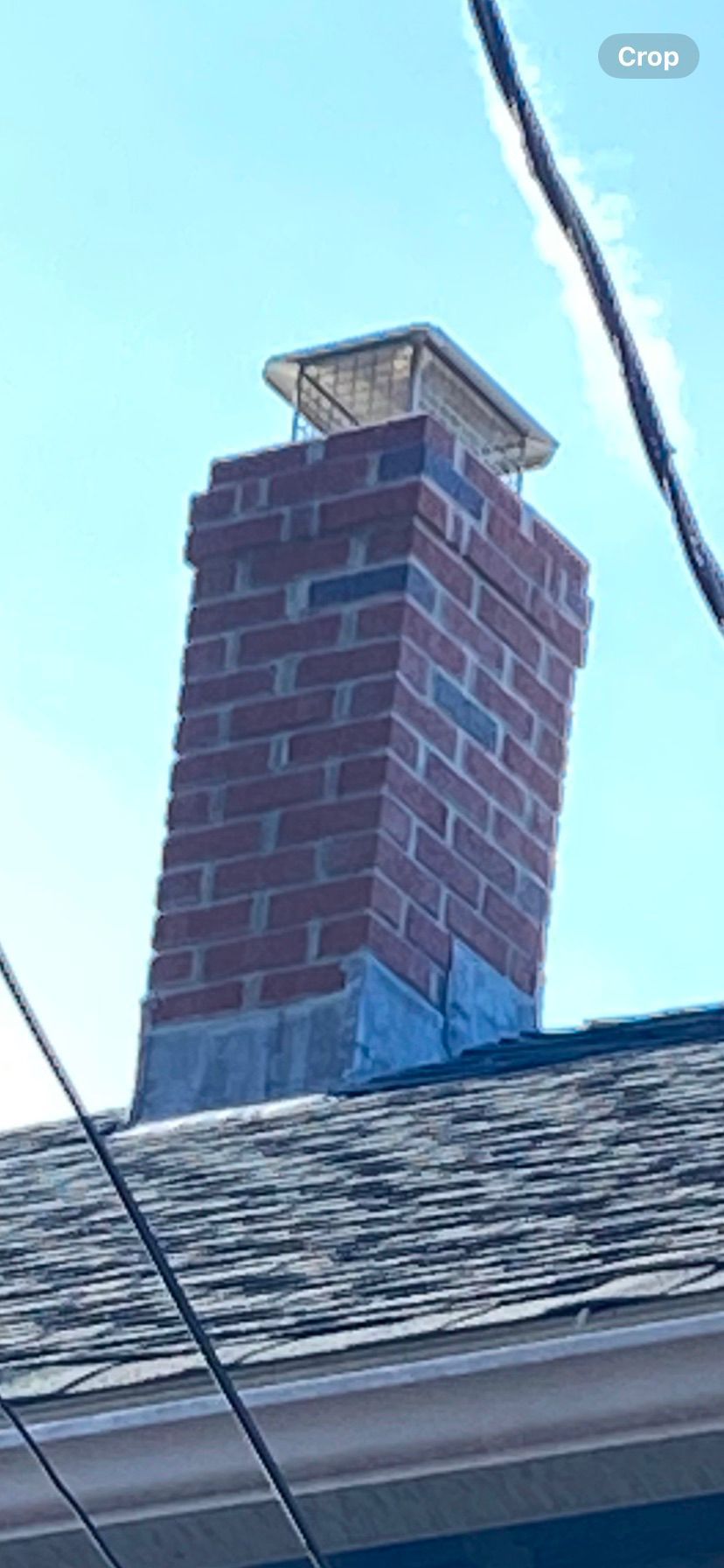 Brick chimney on a shingled roof against a blue sky.