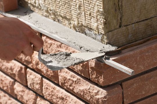 Hand trowel smoothing mortar along a brick wall corner outdoors