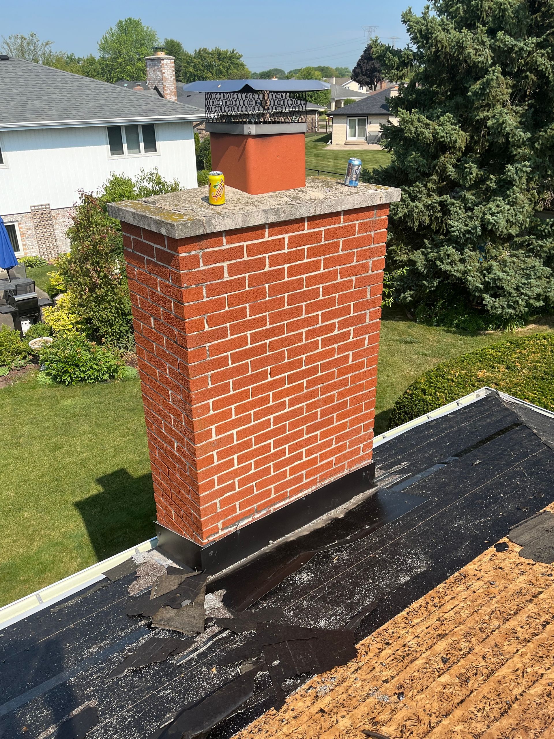 Brick chimney on a black flat roof, surrounded by green grass and trees.