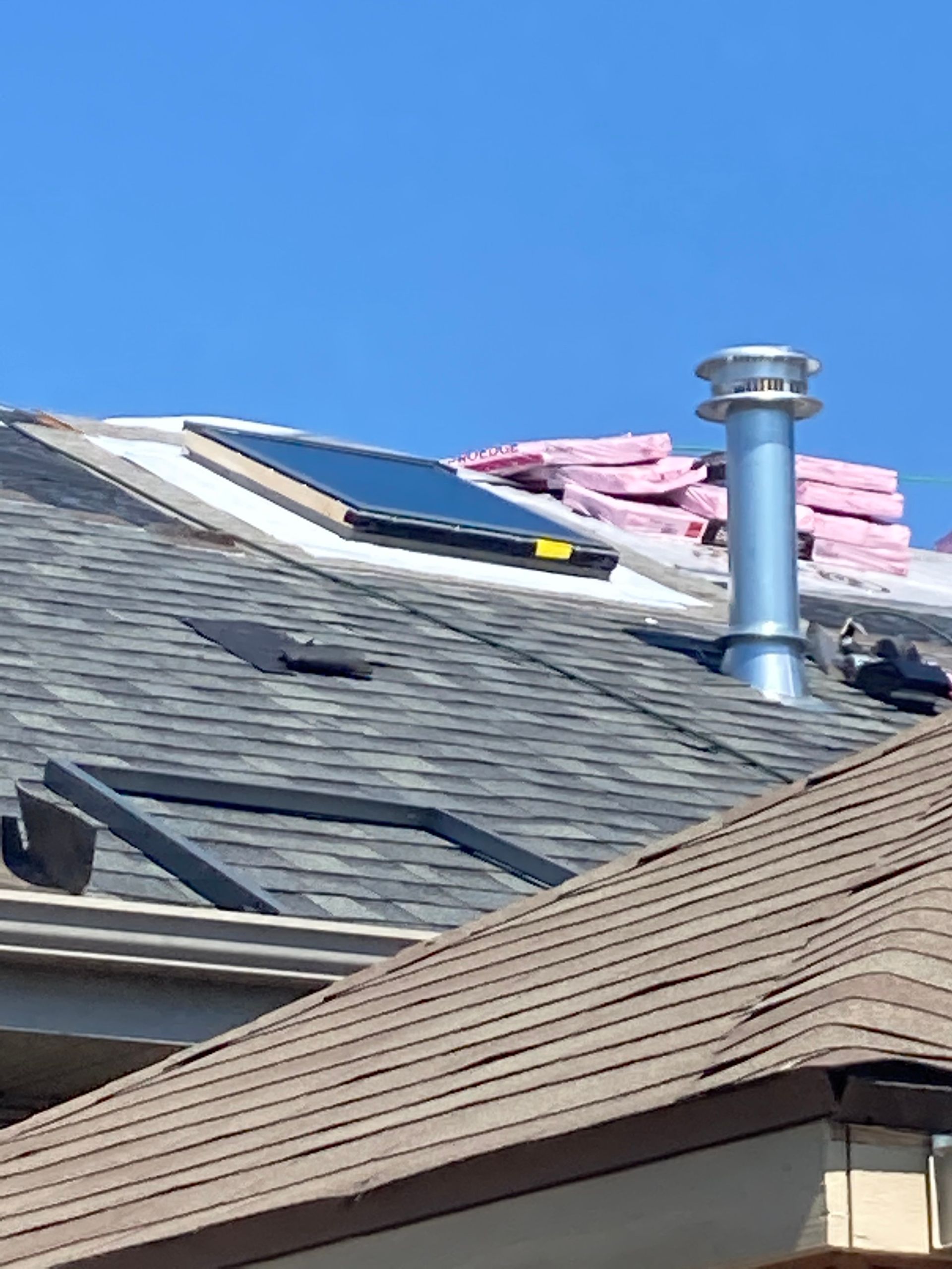 A rooftop with a chimney, skylight, and insulation under a clear, blue sky.