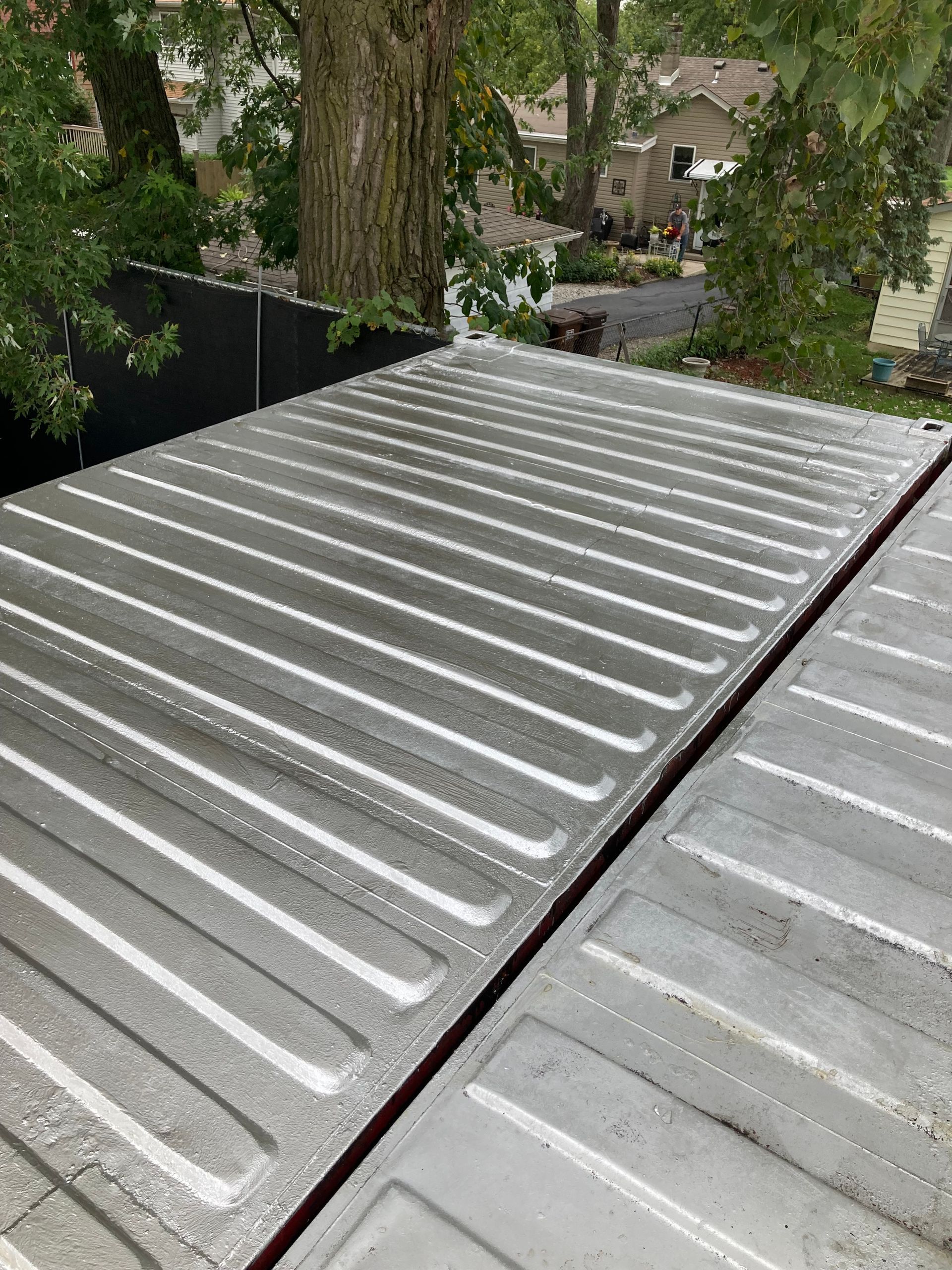 Gray corrugated metal roof, with a large tree in the background.