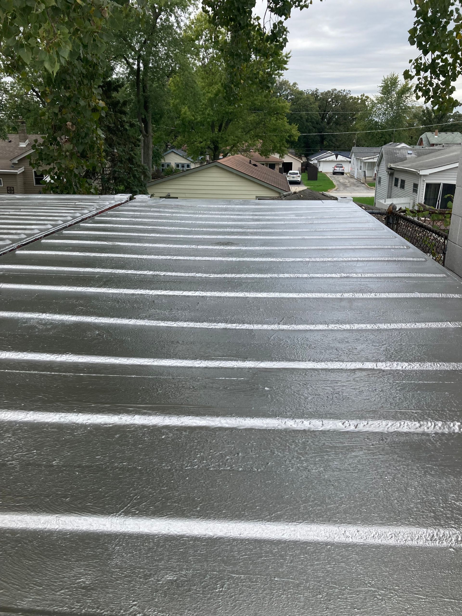 Overhead view of a flat roof with horizontal, gray panels. A street and trees are in the background.