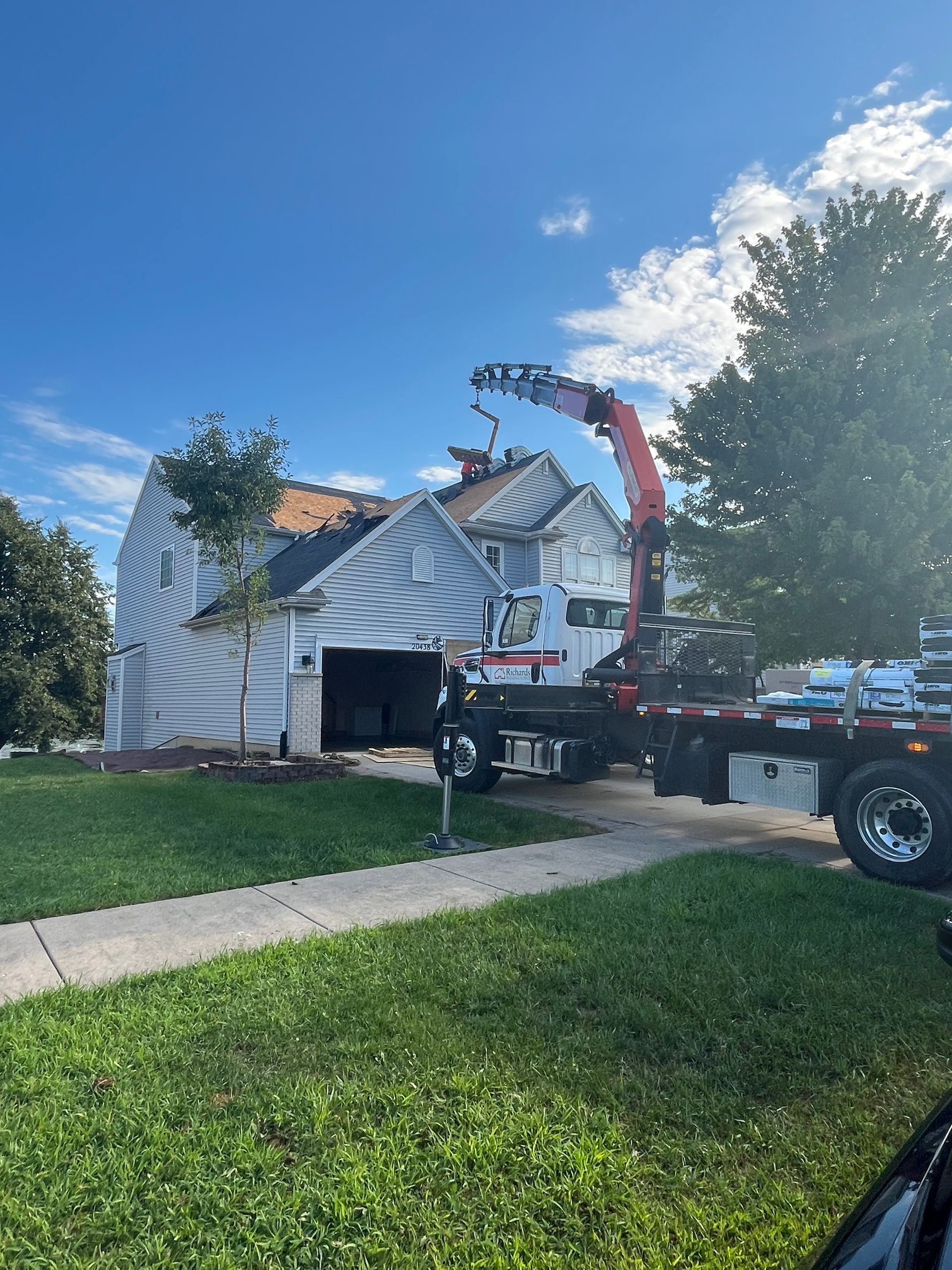 A house with a damaged roof being worked on by a crane truck on a sunny day.