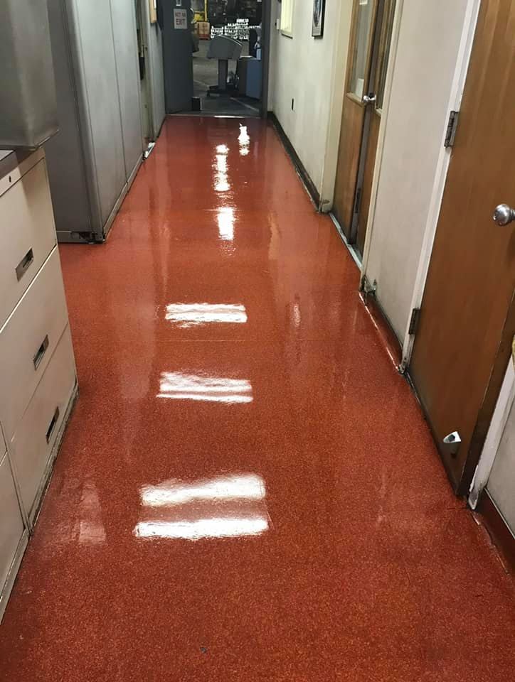 Long hallway with shiny, speckled red floor, cabinets on the left, doors on the right.