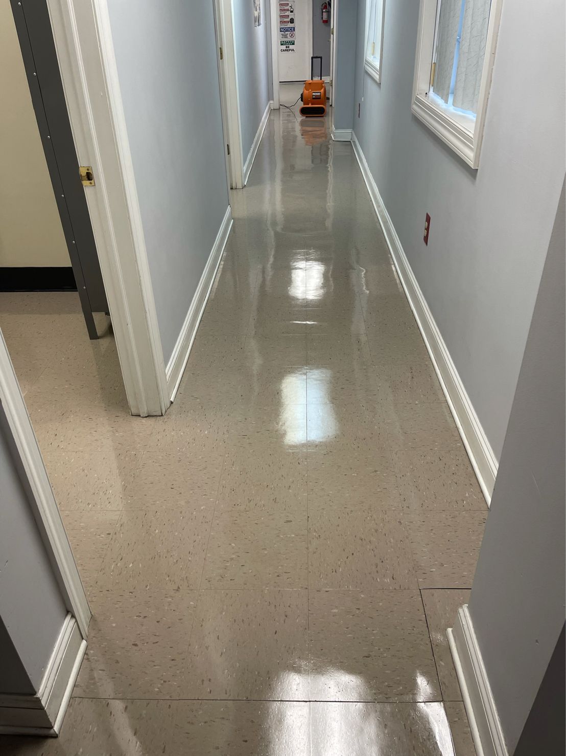 Long, narrow hallway with shiny speckled flooring, light gray walls, and white trim.  A door opens into the hall at the left.