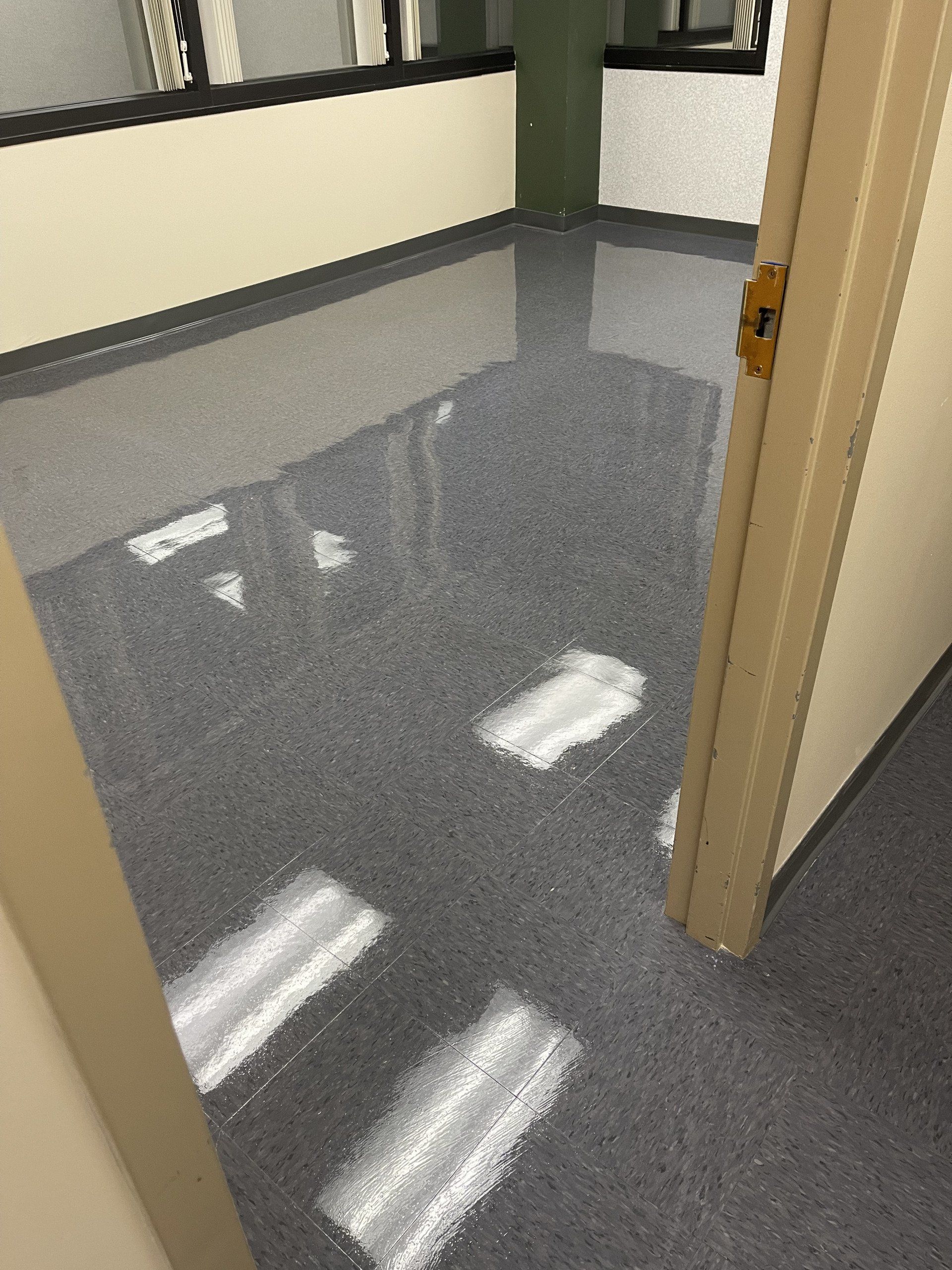 A room with shiny gray speckled floor. The door frame and walls are beige, with windows visible in the background.