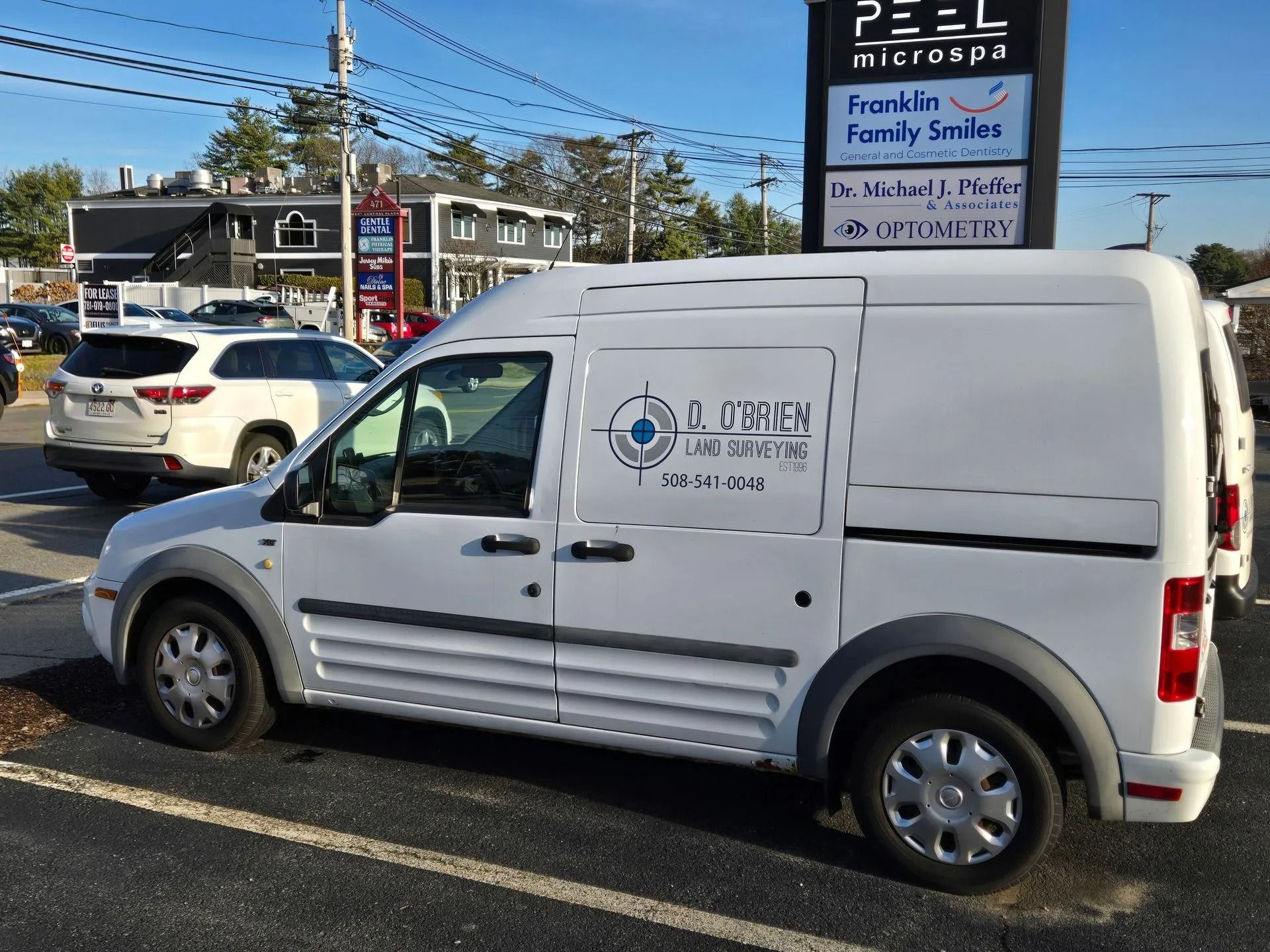 A white work van with a company logo parked in a parking lot next to a commercial building sign.