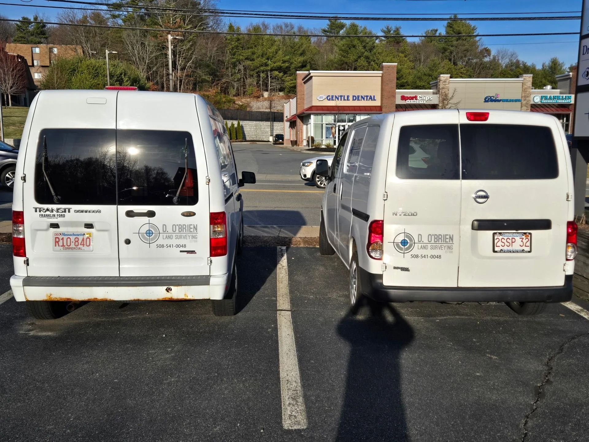Two white commercial vans are parked side-by-side in a parking lot, both featuring the same business logo on the rear doors.