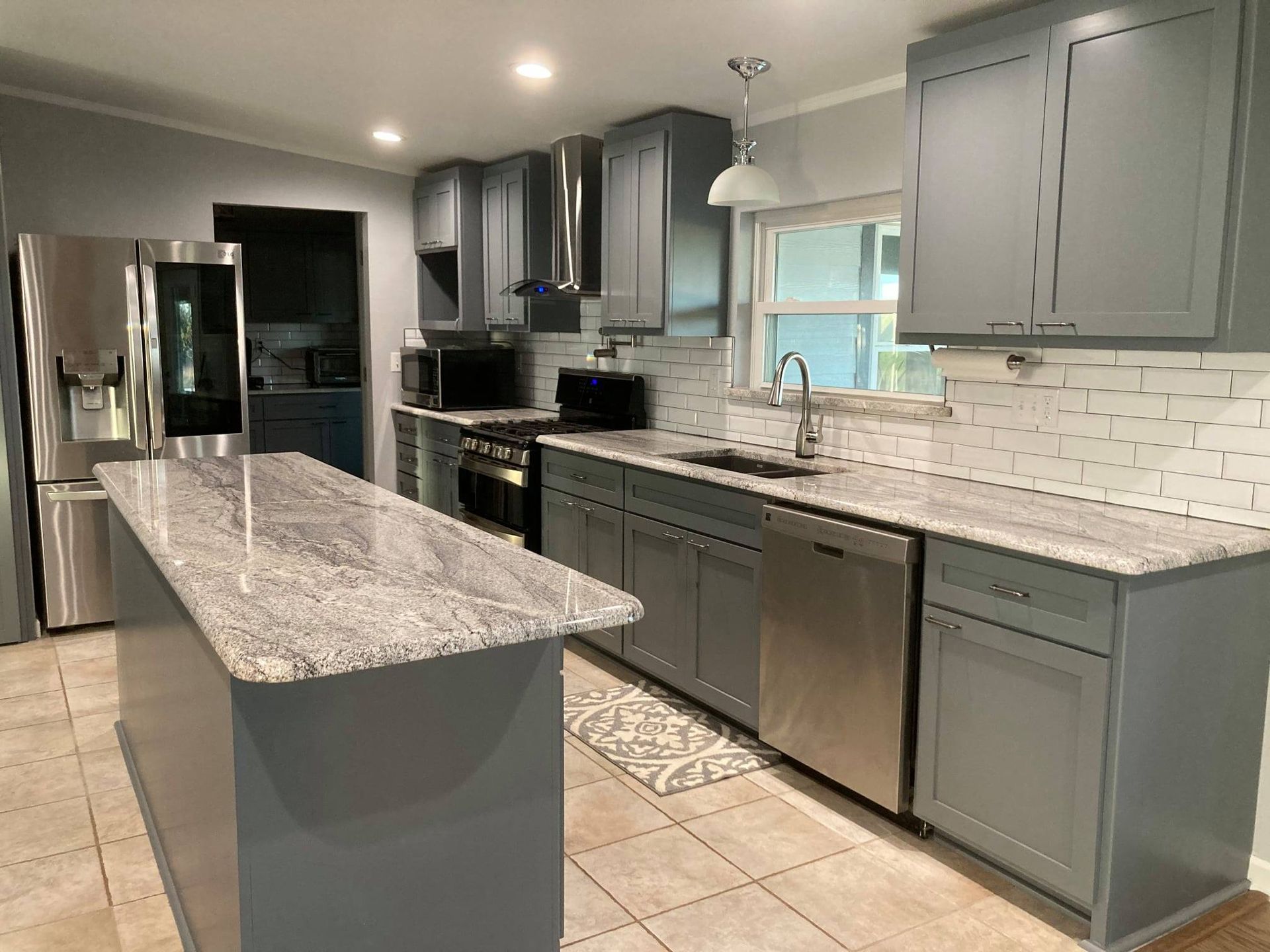 A kitchen with gray cabinets, granite counter tops, stainless steel appliances and a large island