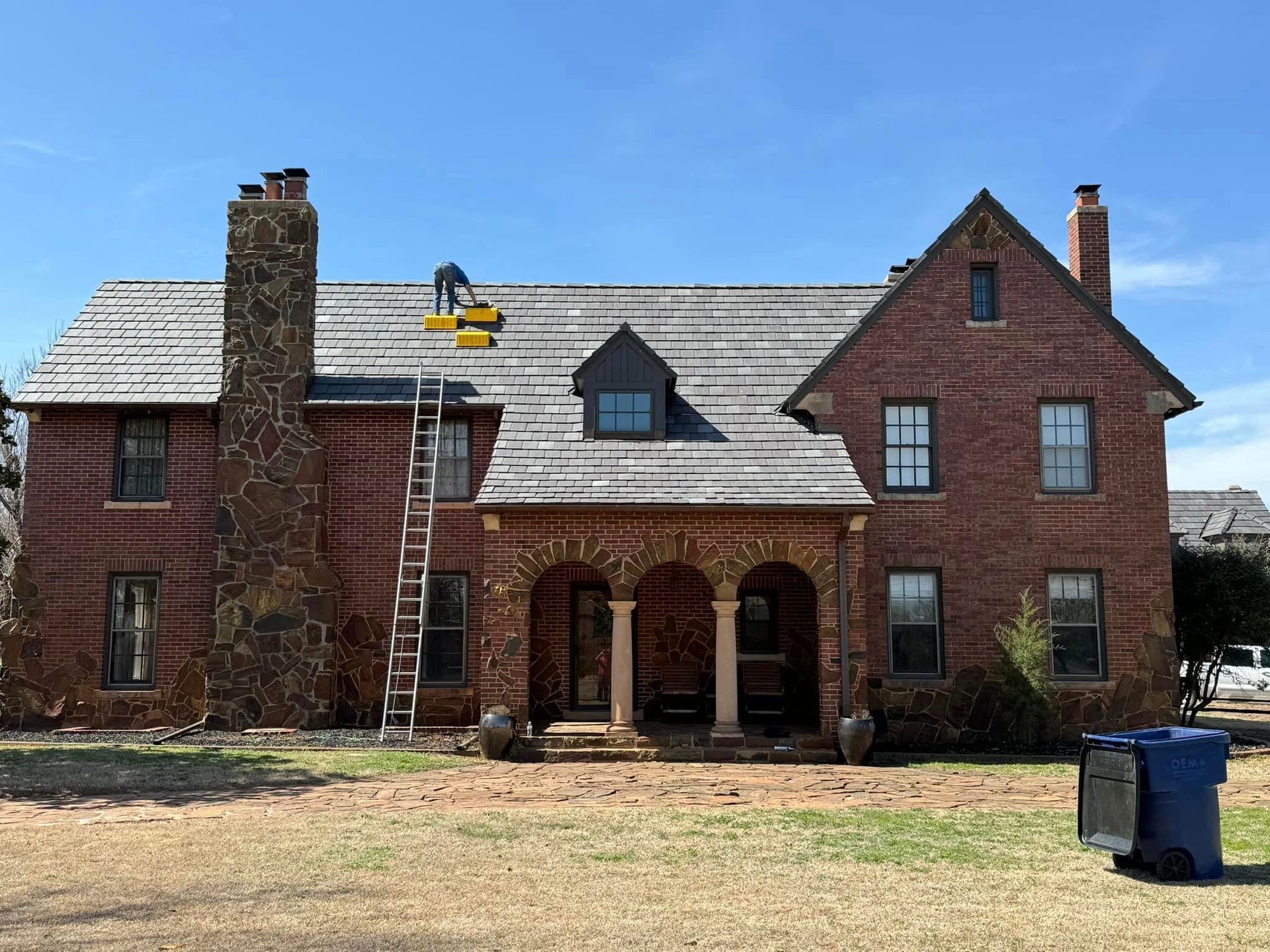A large brick house with a blue trash can in front of it