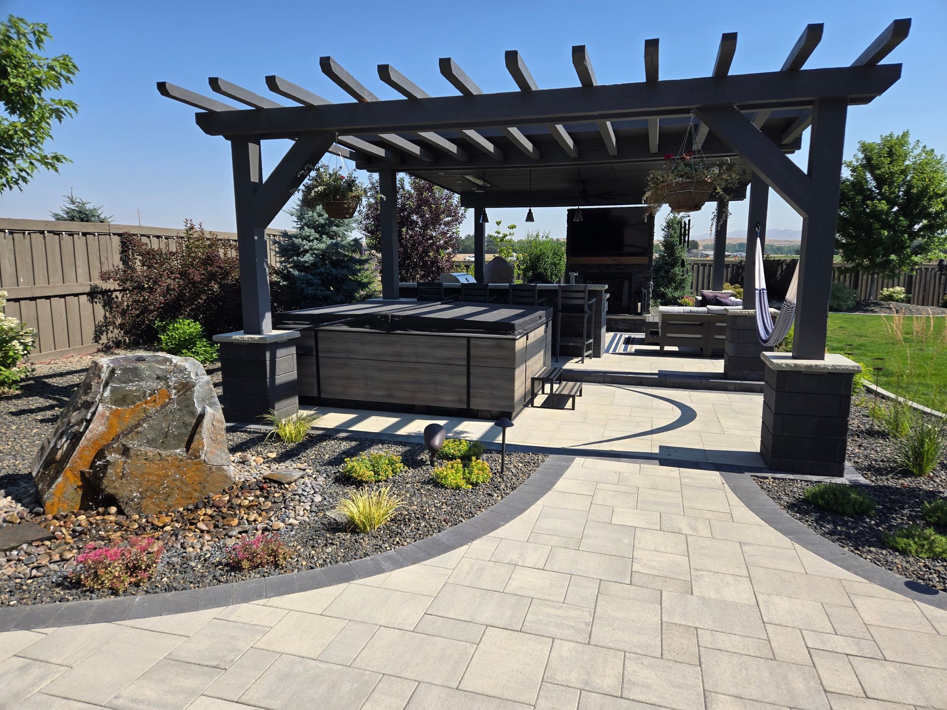 Backyard patio with a wooden pergola, seating area, and landscaped garden path under a clear blue sky