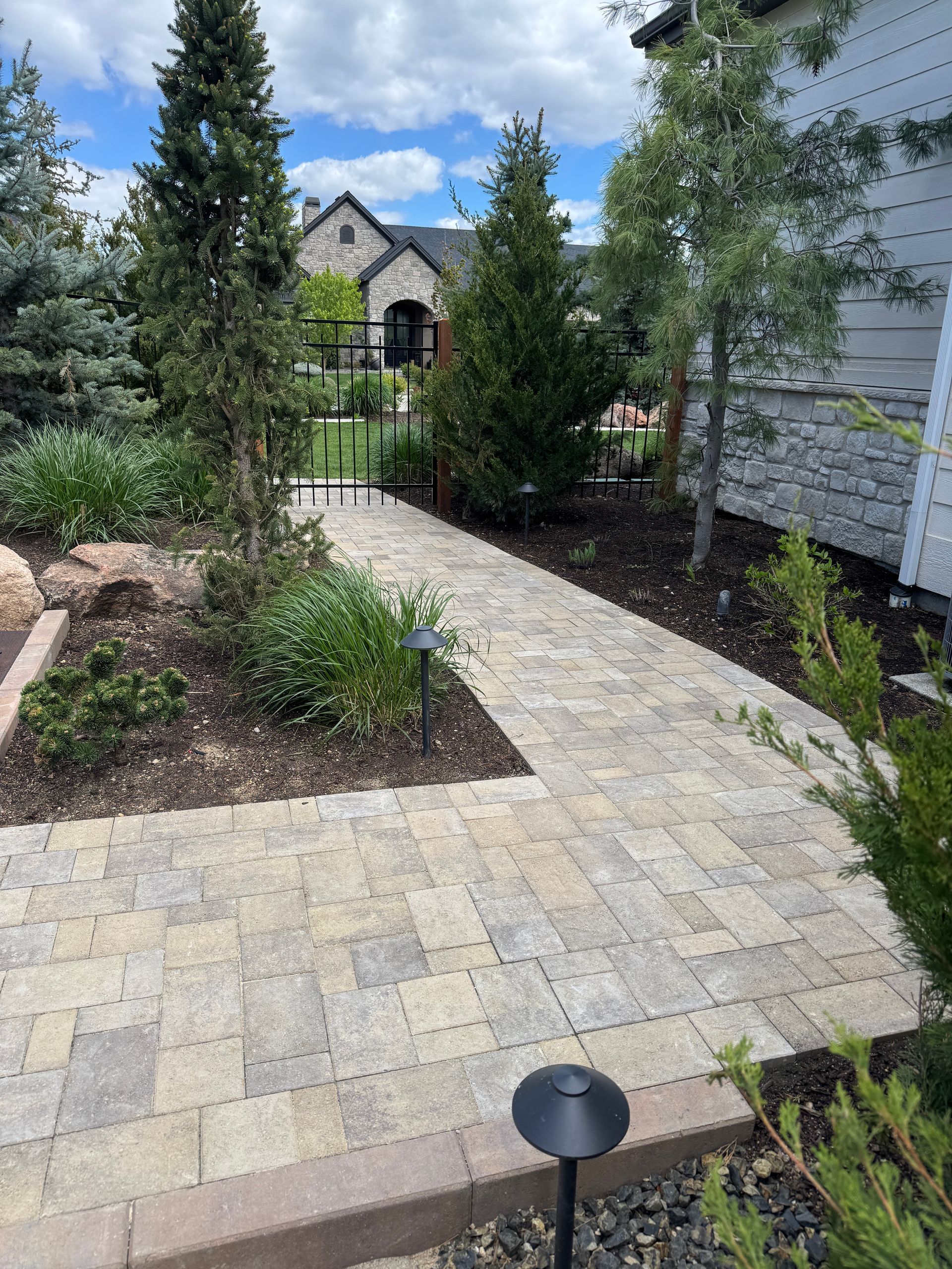 Stone garden path leading to a house, bordered by shrubs and trees under a blue sky