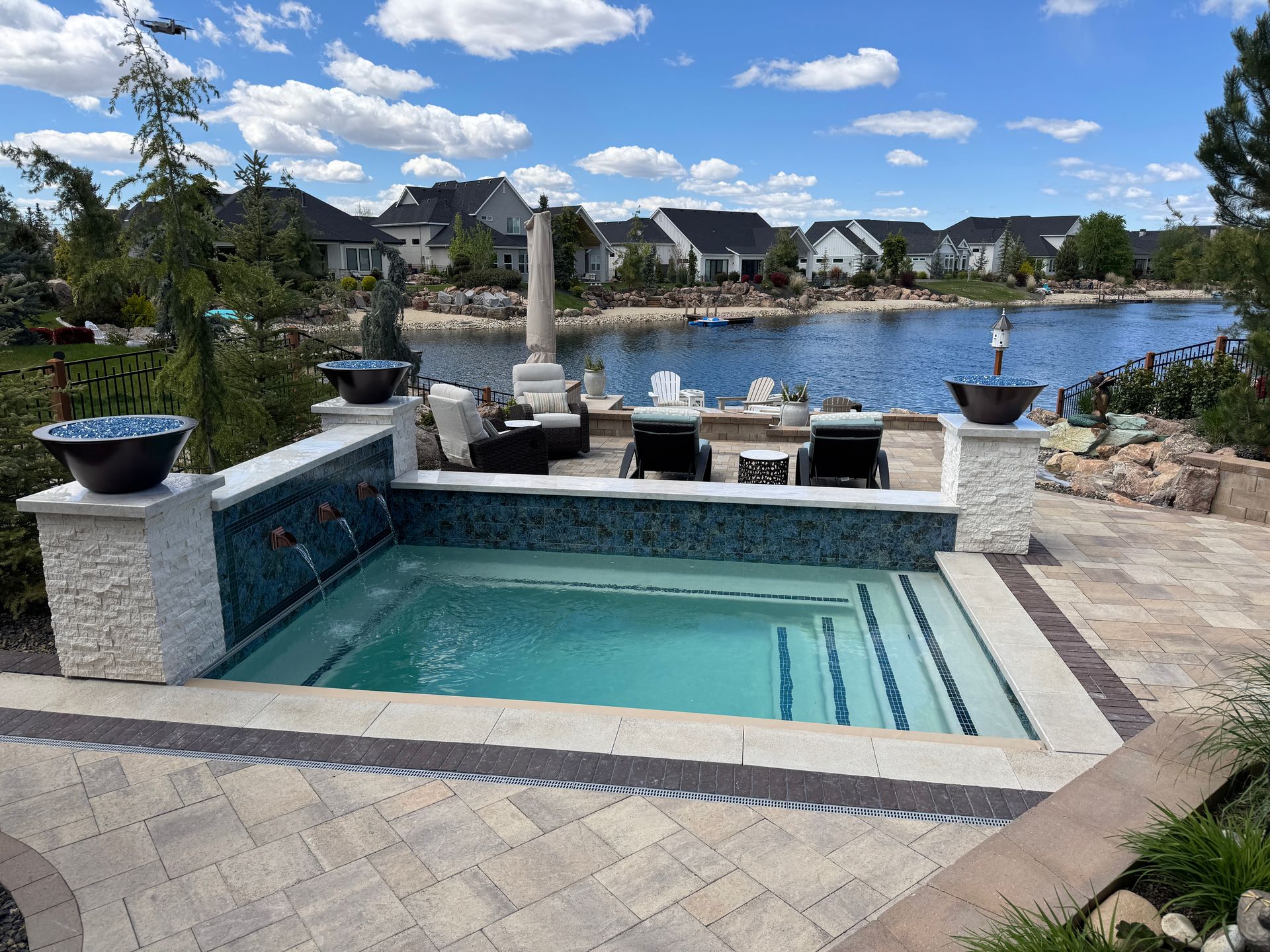 Backyard pool spa with stone deck overlooking a lake and waterfront homes