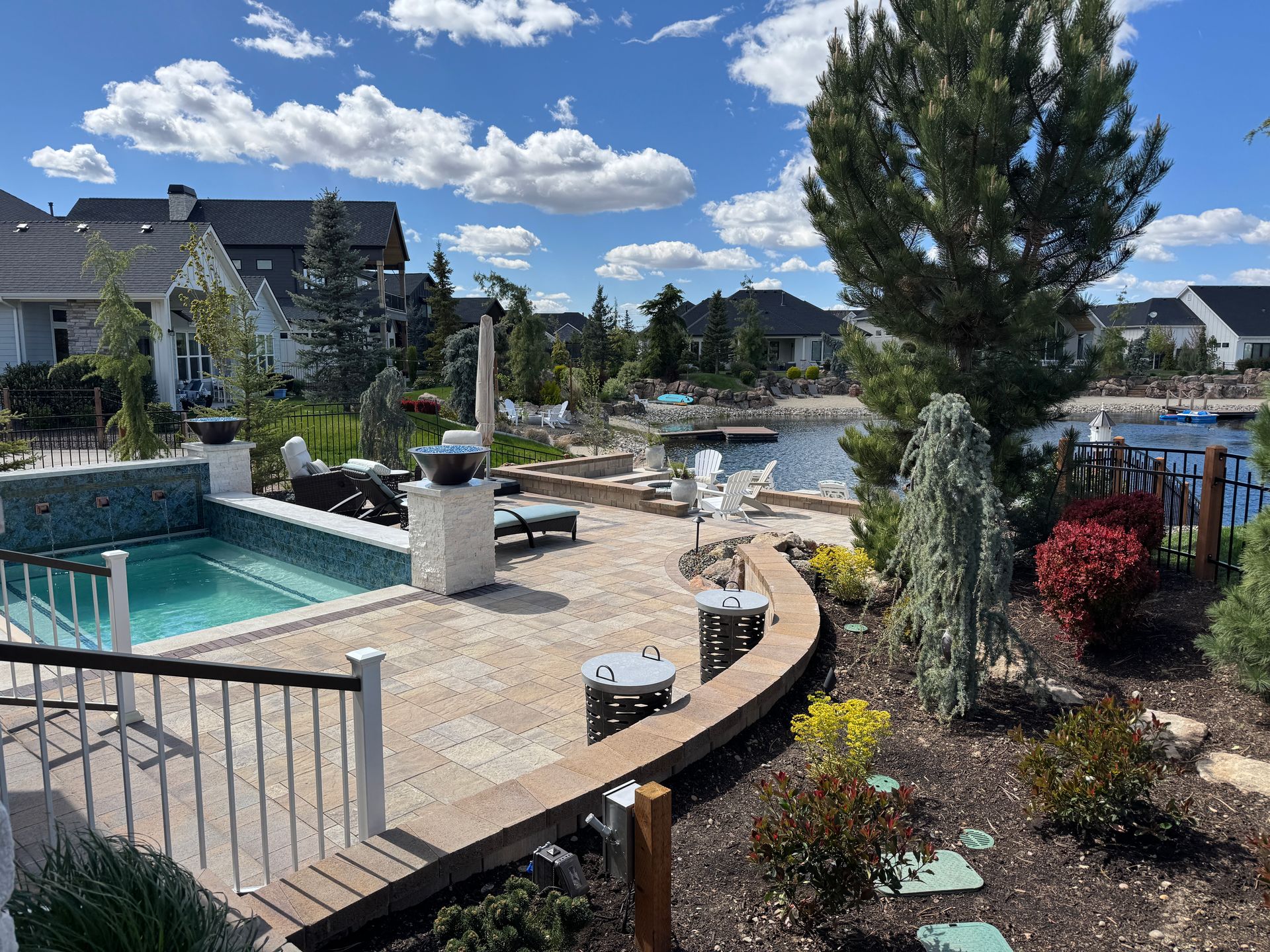 Backyard pool and patio with curved stone wall, lounge chairs, landscaping, and cloudy blue sky