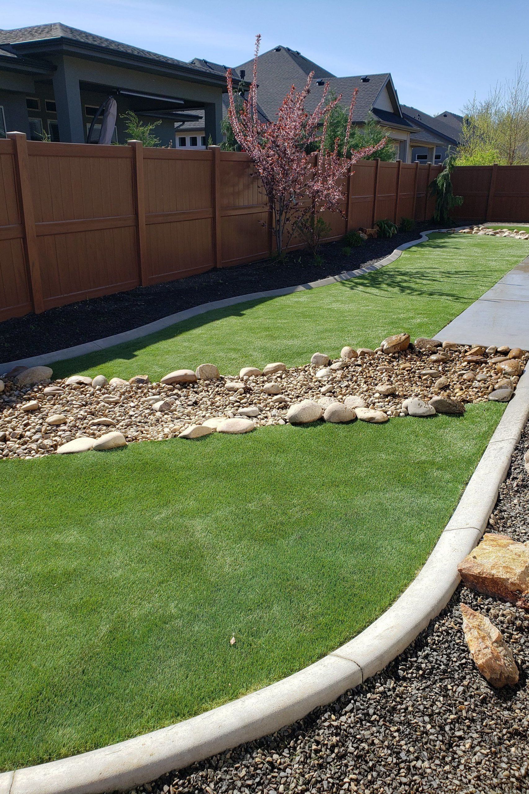 Landscaped front yard with green lawn, rock border, and a brown wooden fence along the side.