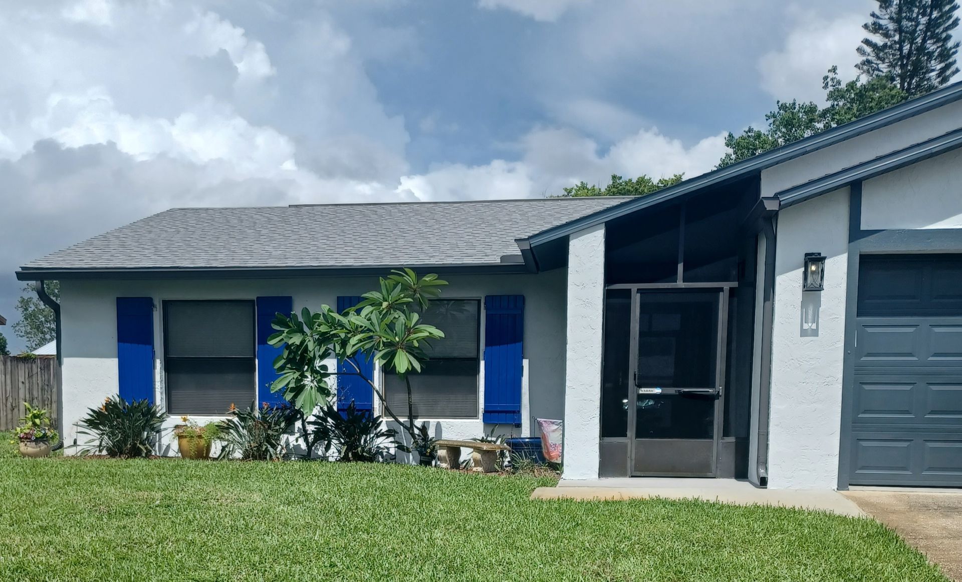 Single-story house with blue shutters, garage, and front lawn under cloudy skies