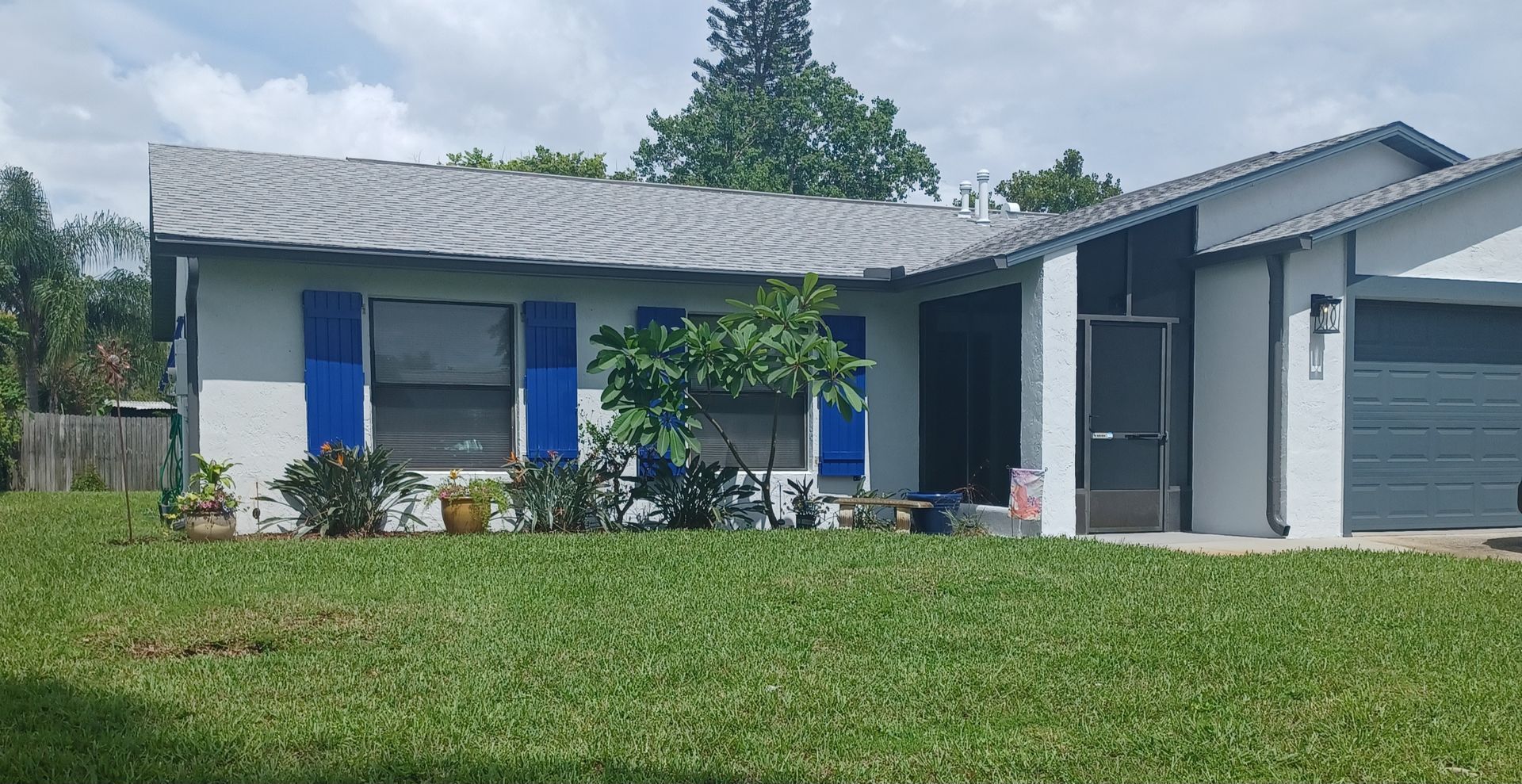 Single-story blue-gray house with a front lawn, trees, and a garage in daylight