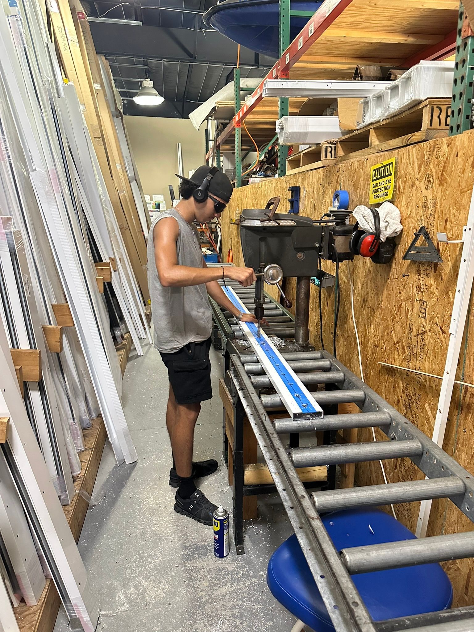 Person using a miter saw in a workshop, surrounded by stacked lumber and tools.