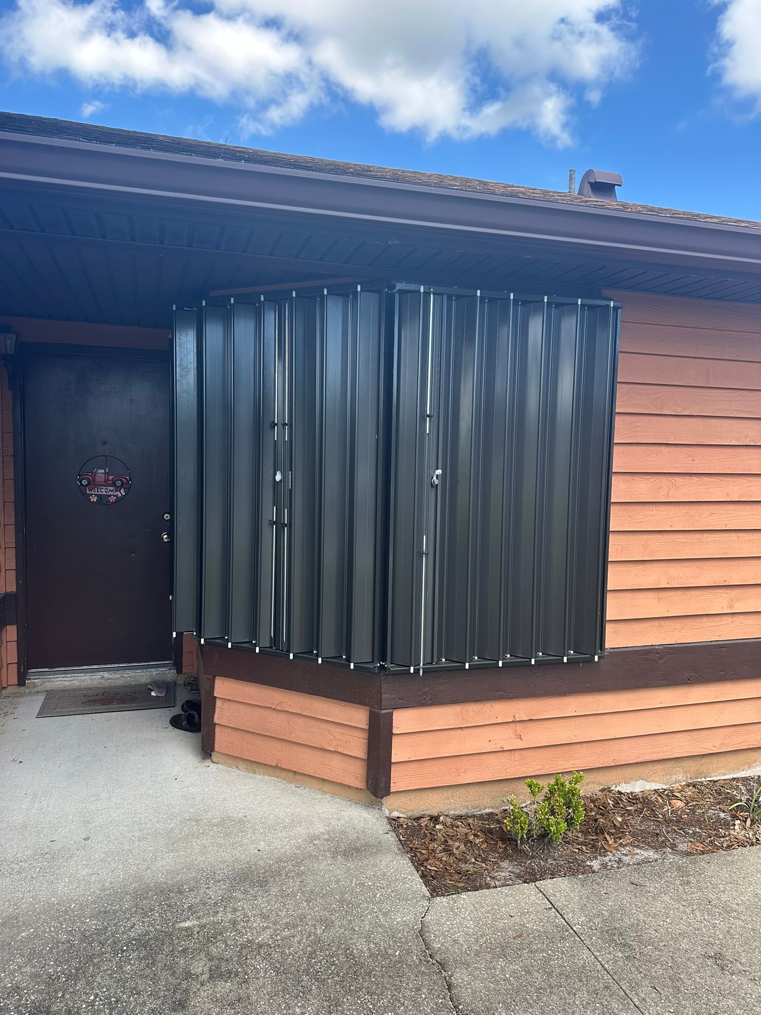Modern house exterior with black vertical slat porch enclosure and wood siding under a blue sky