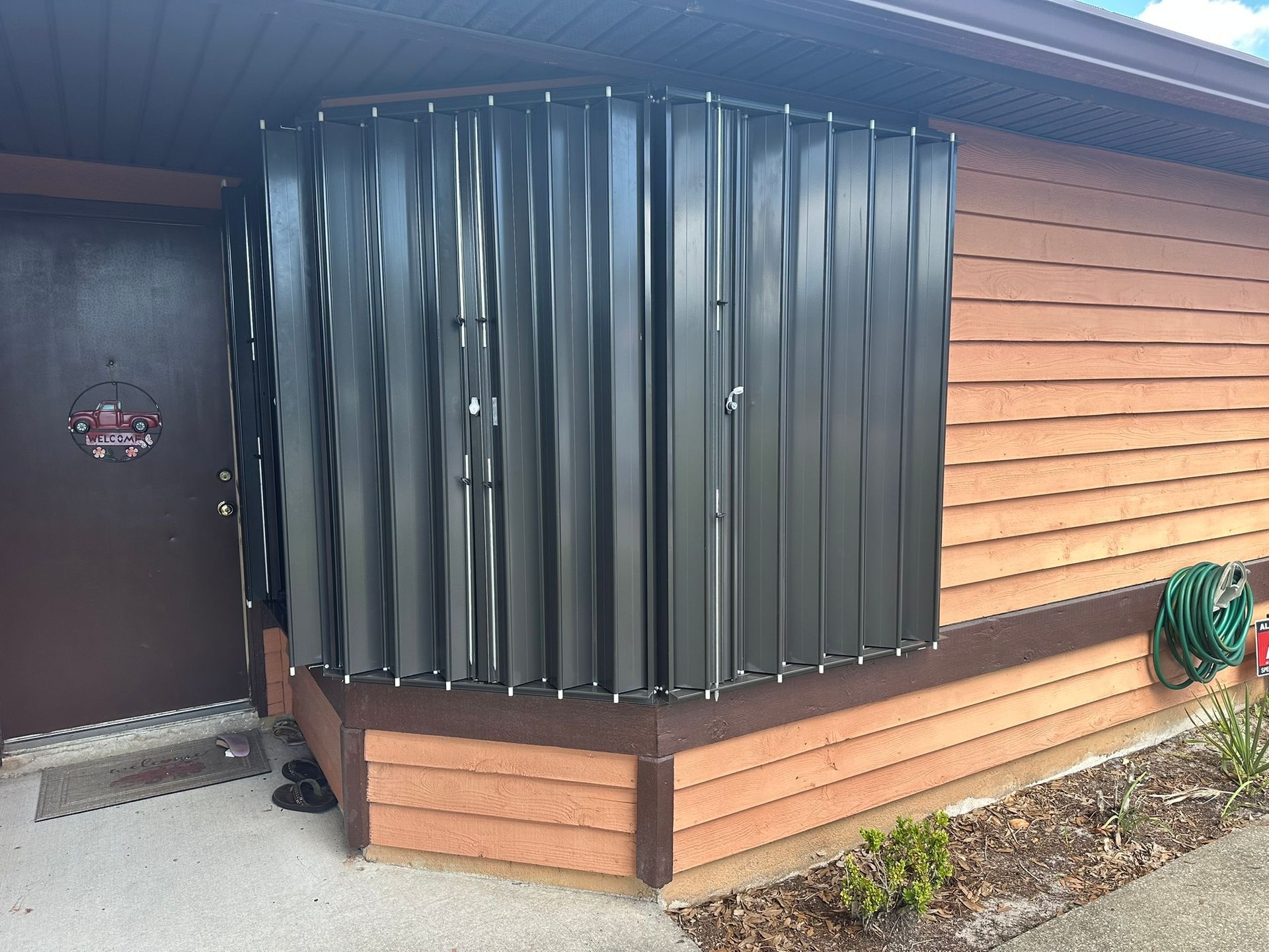 Dark green window awning on a tan house exterior beside a brown door and siding