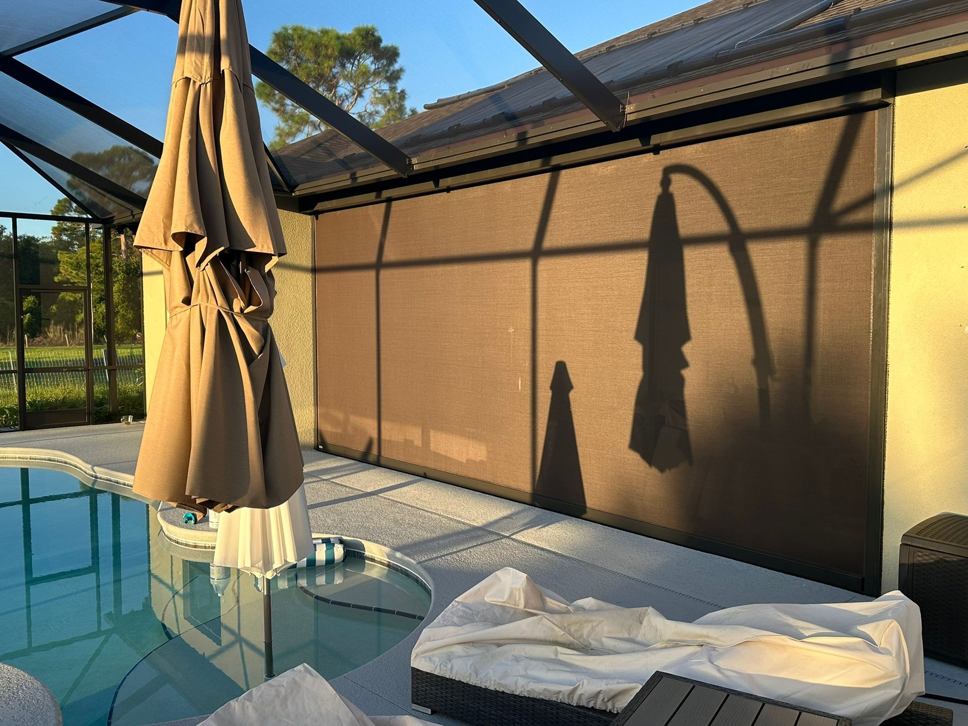 Backyard pool with closed beige umbrella, lounge chair, and sunlit tan wall reflection