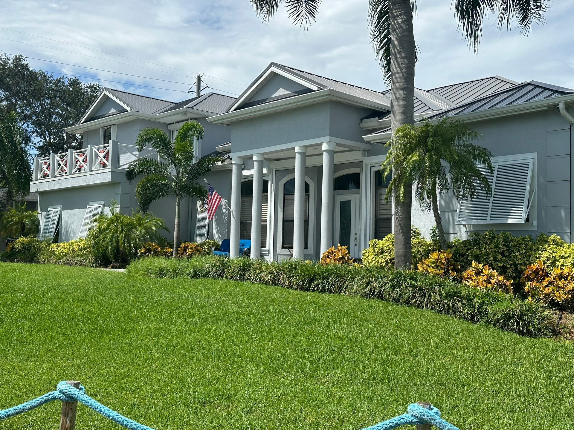White tropical-style house with columns, palm trees, and a green lawn under a partly cloudy sky