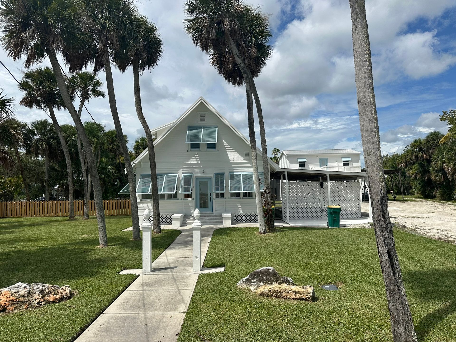 White A-frame beach house with porch, palms, and a walkway across a grassy yard