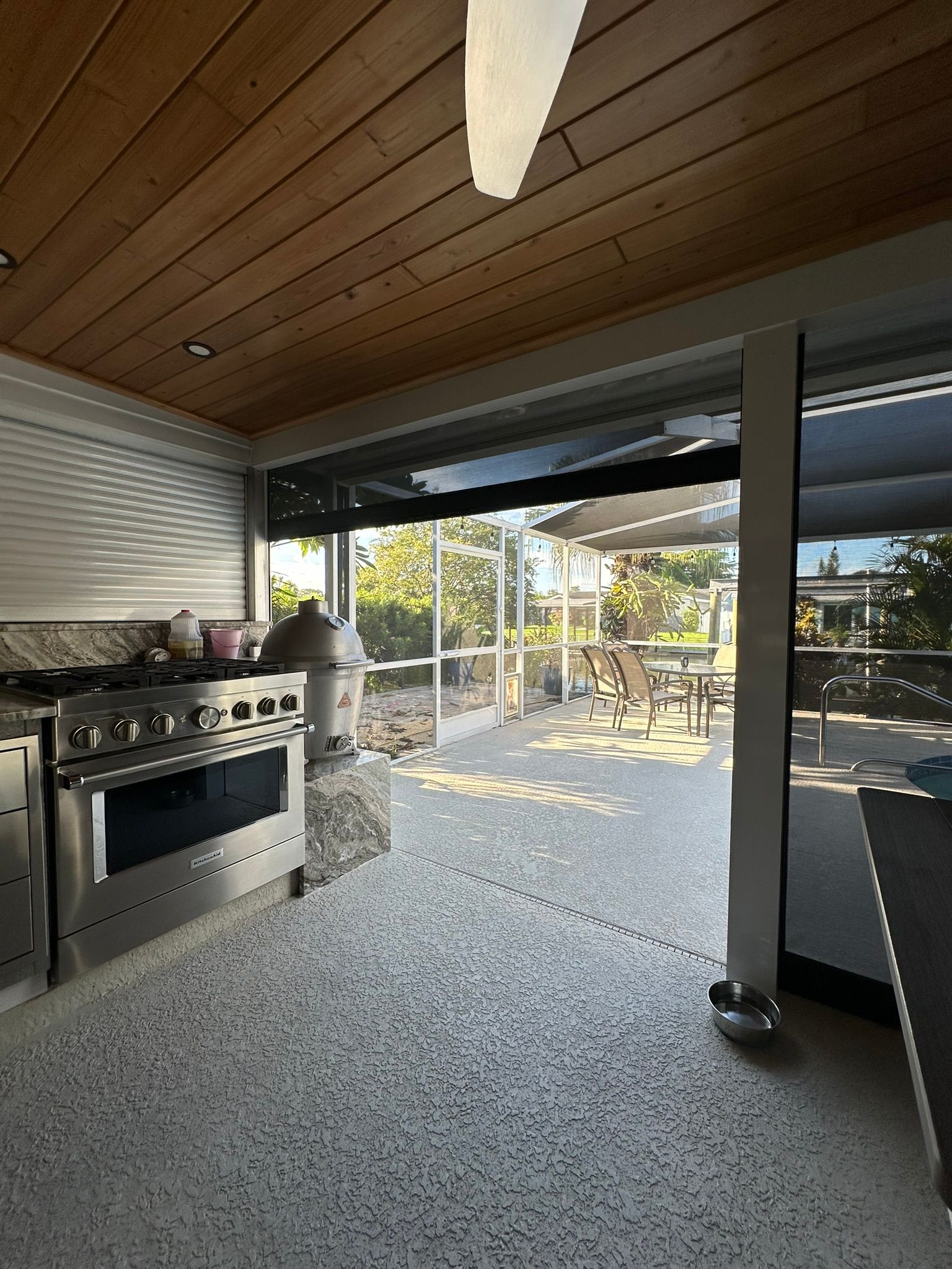 Covered outdoor patio with grill, ceiling fan, and open seating area overlooking a backyard.