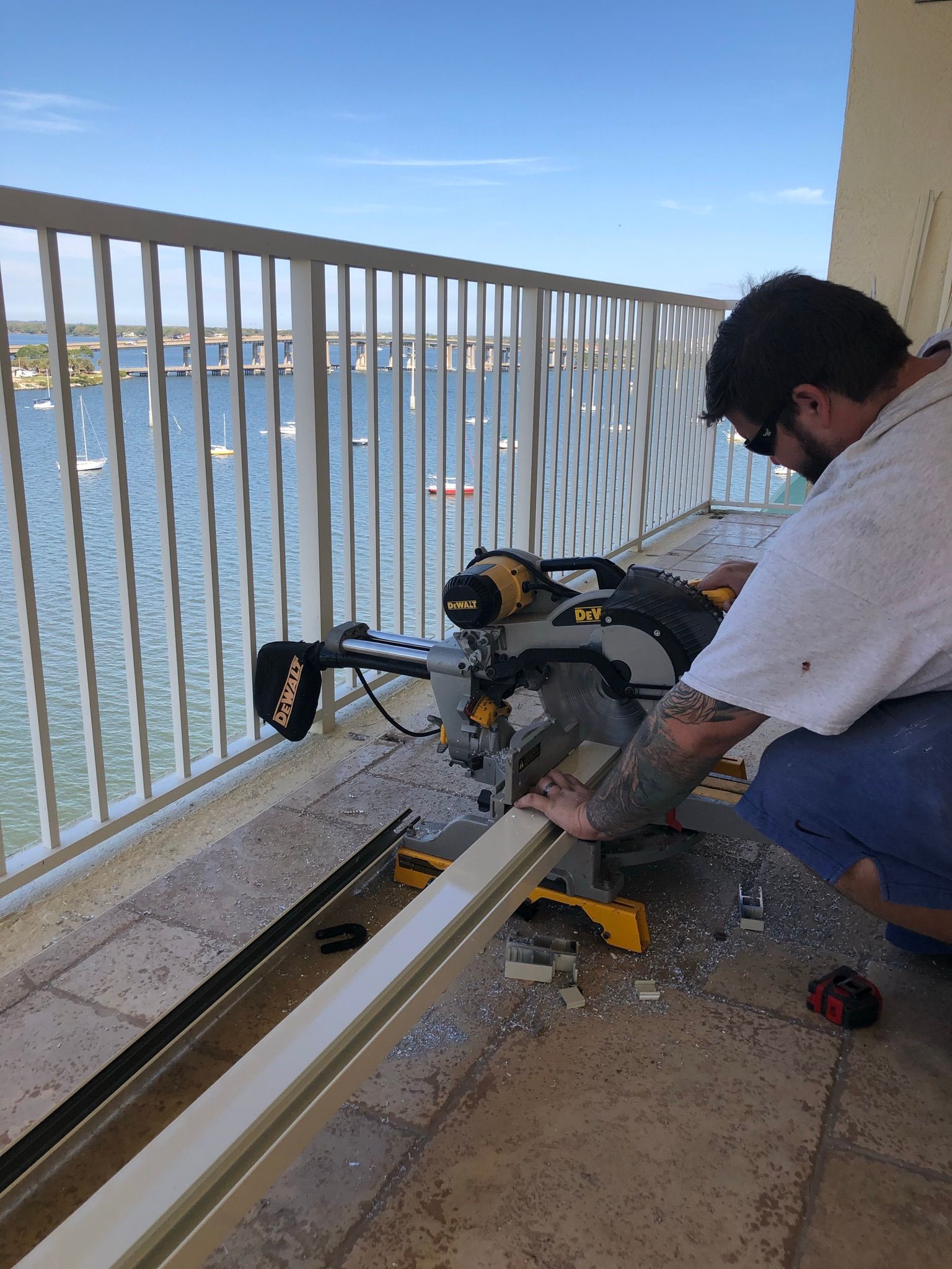 Person using a circular saw to cut a long metal beam on a balcony beside the water.