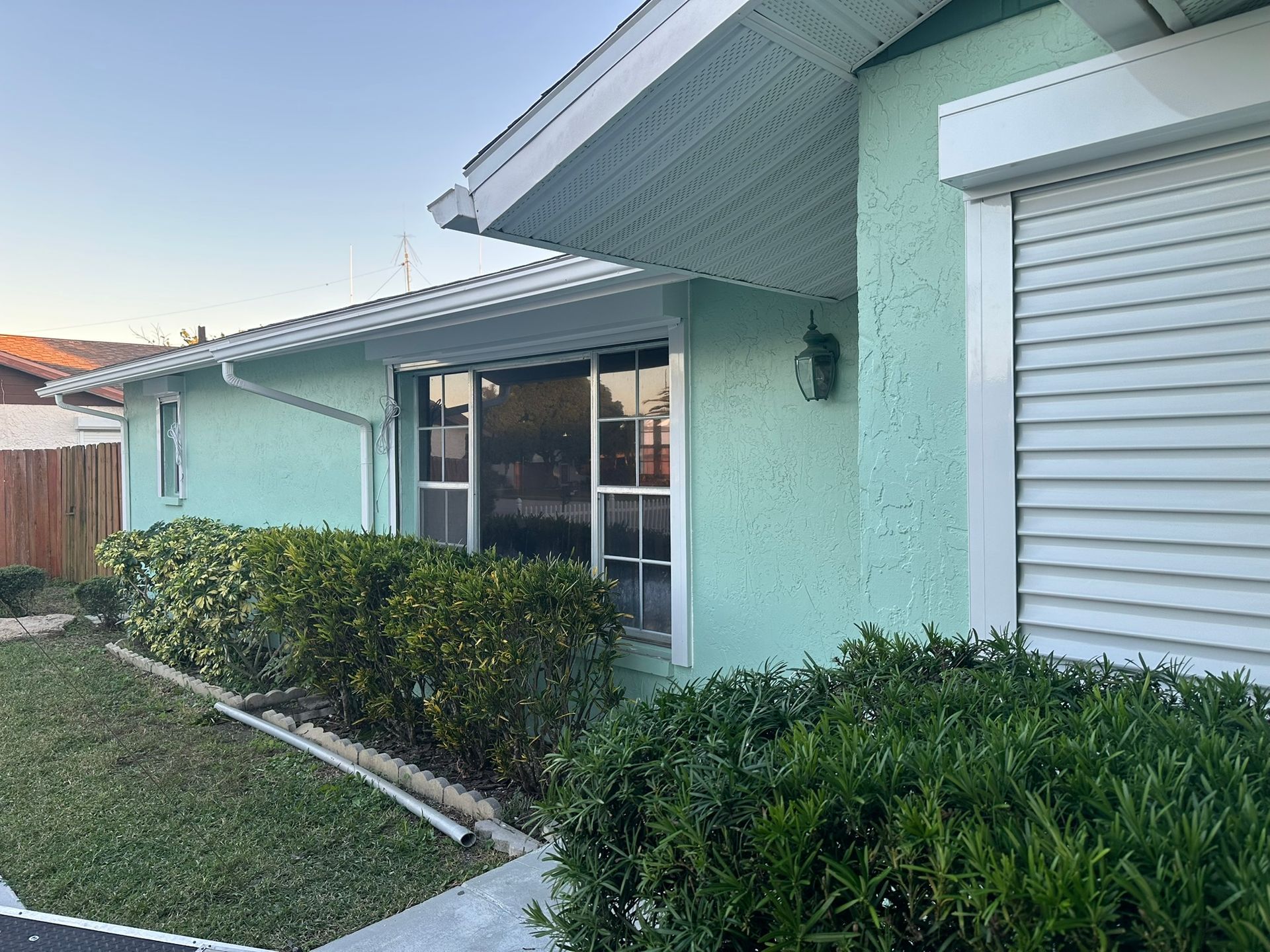 Suburban house exterior with mint-green walls, hedge, and white garage door