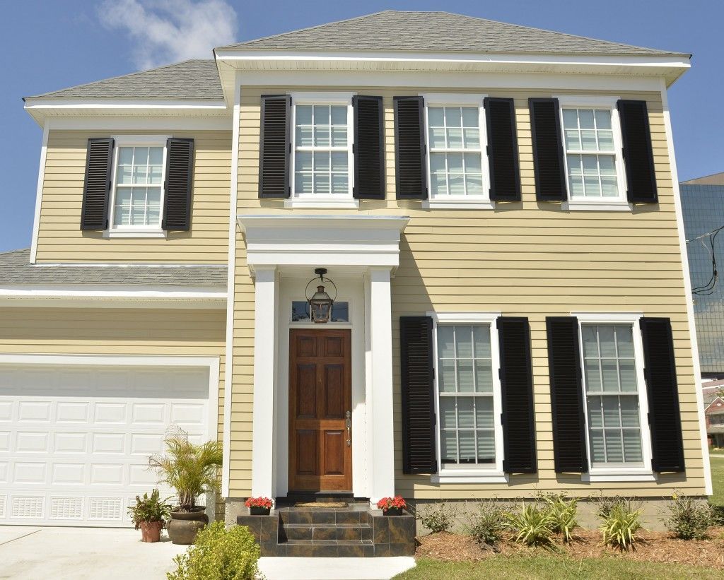 Two-story beige suburban house with white trim, black shutters, and a garage