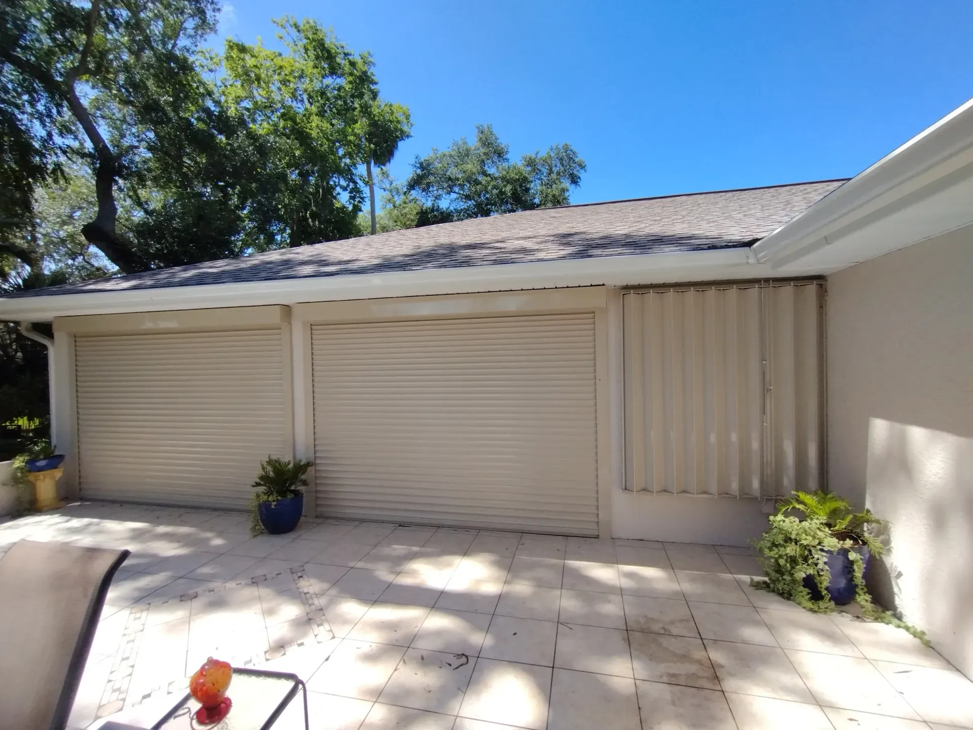 Two garage doors beside a small patio with potted plants under a sunny roofline