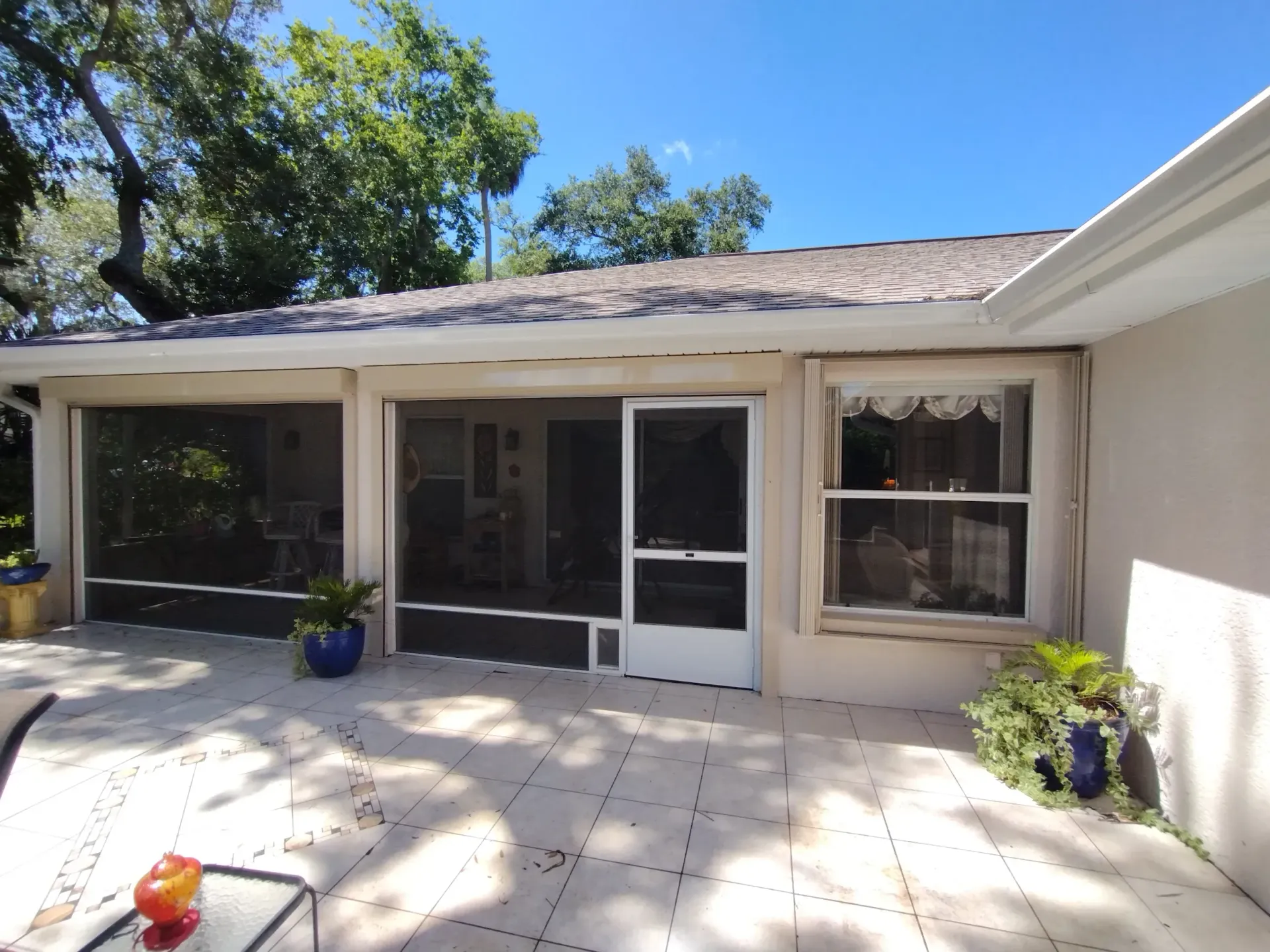 Outdoor patio with screened porch, white sliding doors, potted plants, and bright sunlight