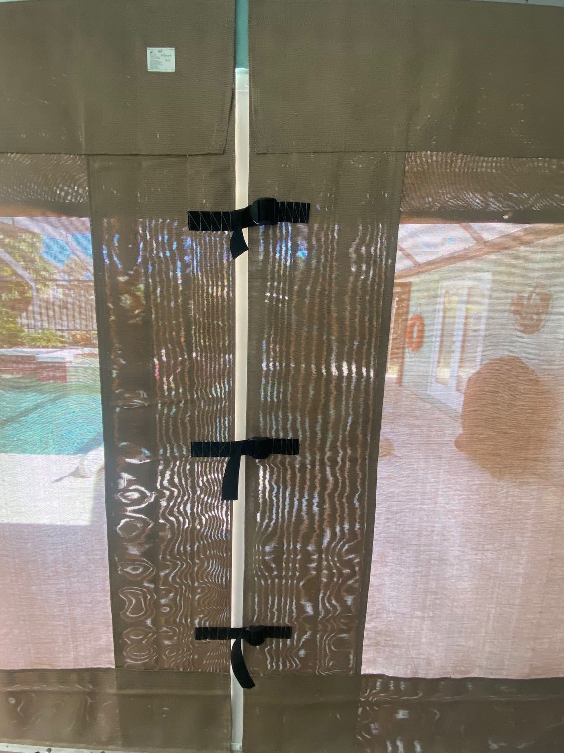 Bamboo privacy curtain with black ties, covering a bright outdoor patio and pool view