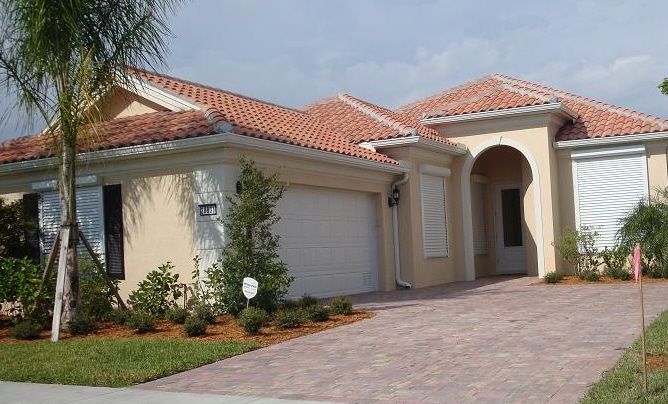 Single-story house with red tile roof, arched entryway, and brick driveway surrounded by palm landscaping